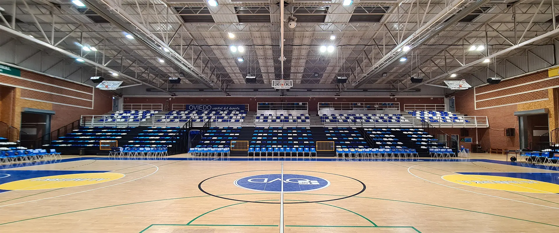 Frente grada de la pista polideportiva de dos niveles con asientos azules y blancos. Zonas pista azul y amarillo