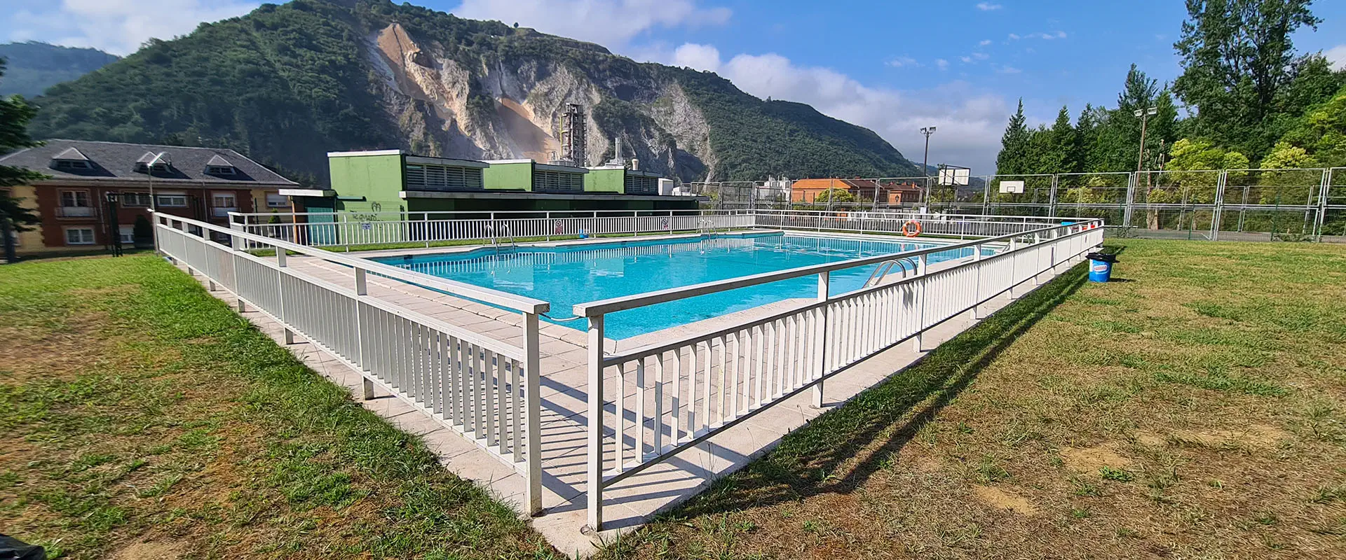 vista de la pisicna, detrás el edificio de servicios, tejados de viviendas colindantes y una montaña