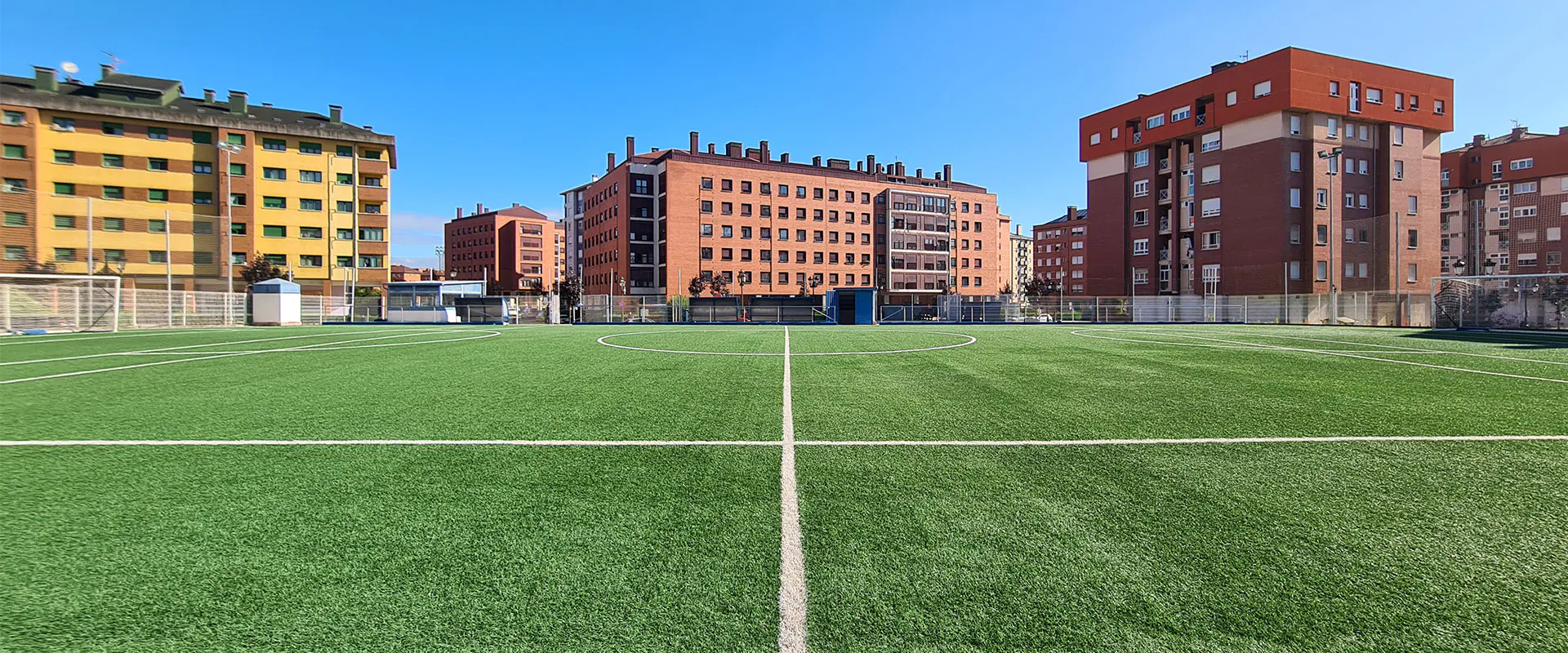 Terreno de juego a ras de césped. Línea del centro del campo en primer plano. Edificios al fondofondo