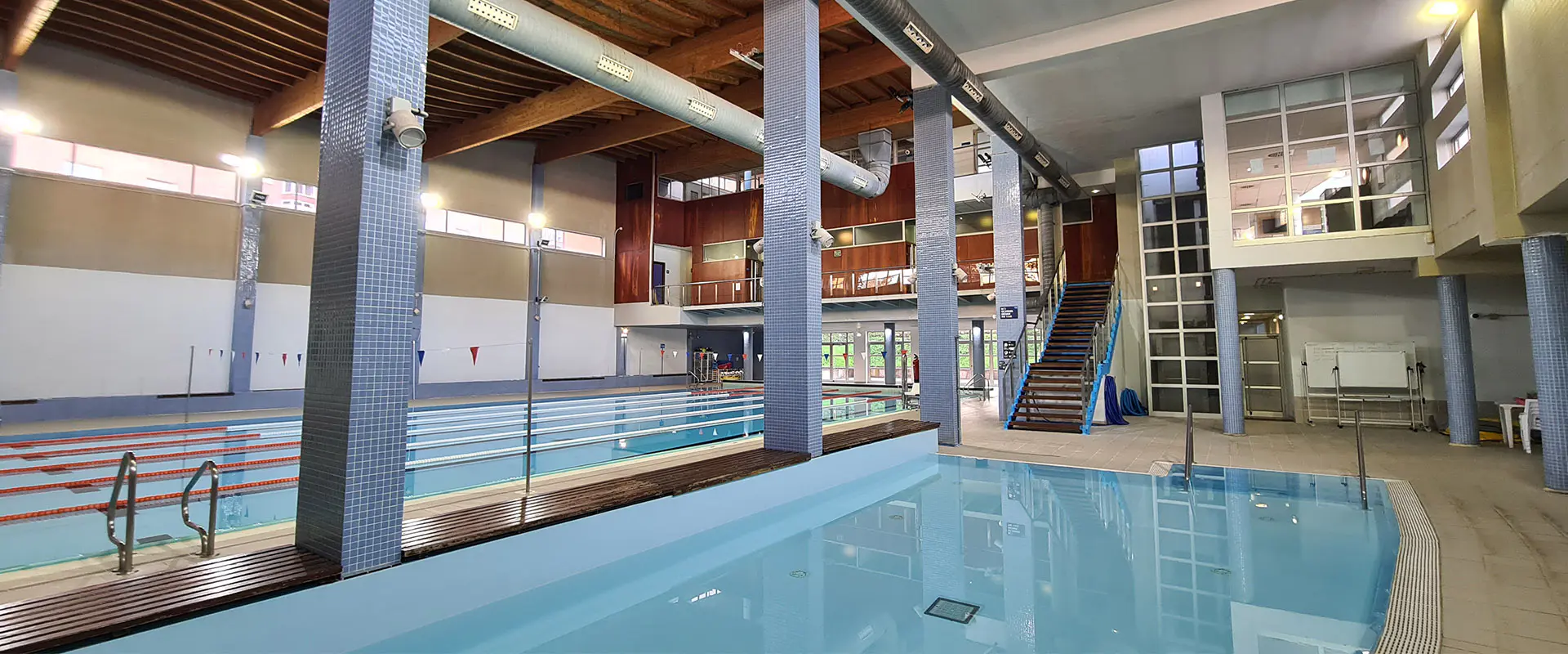 Piscina de aprendizaje en primer plano. Piscina de nado a la izquierda. Al fondo, escaleras de acceso al piso superior