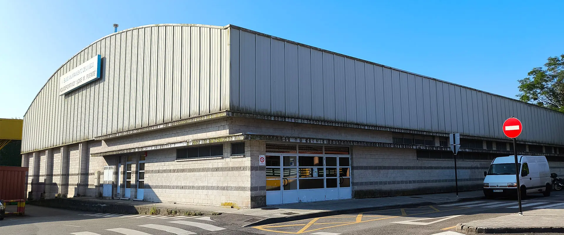 Edificio de bloques de hormigón y tejado metálico. La entrada tiene puertas grandes de color blanco y con cristales
