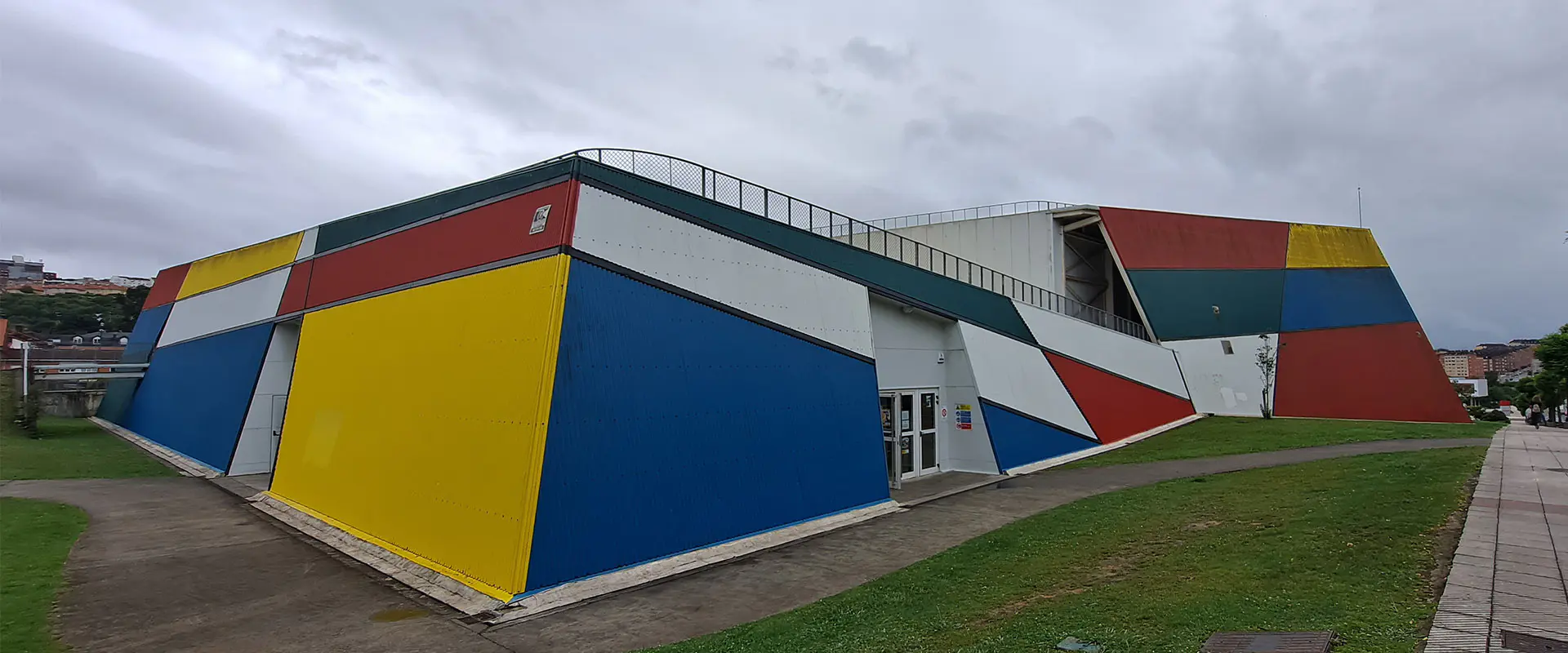 Vista exterior del edificio, con la entrada principal, caminos de acceso y zonas verdes