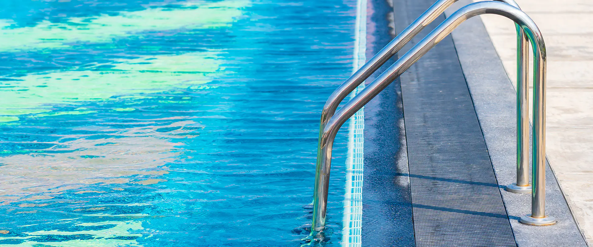 Vista parcial de una piscina con agua, con detalle de las barandillas de acceso