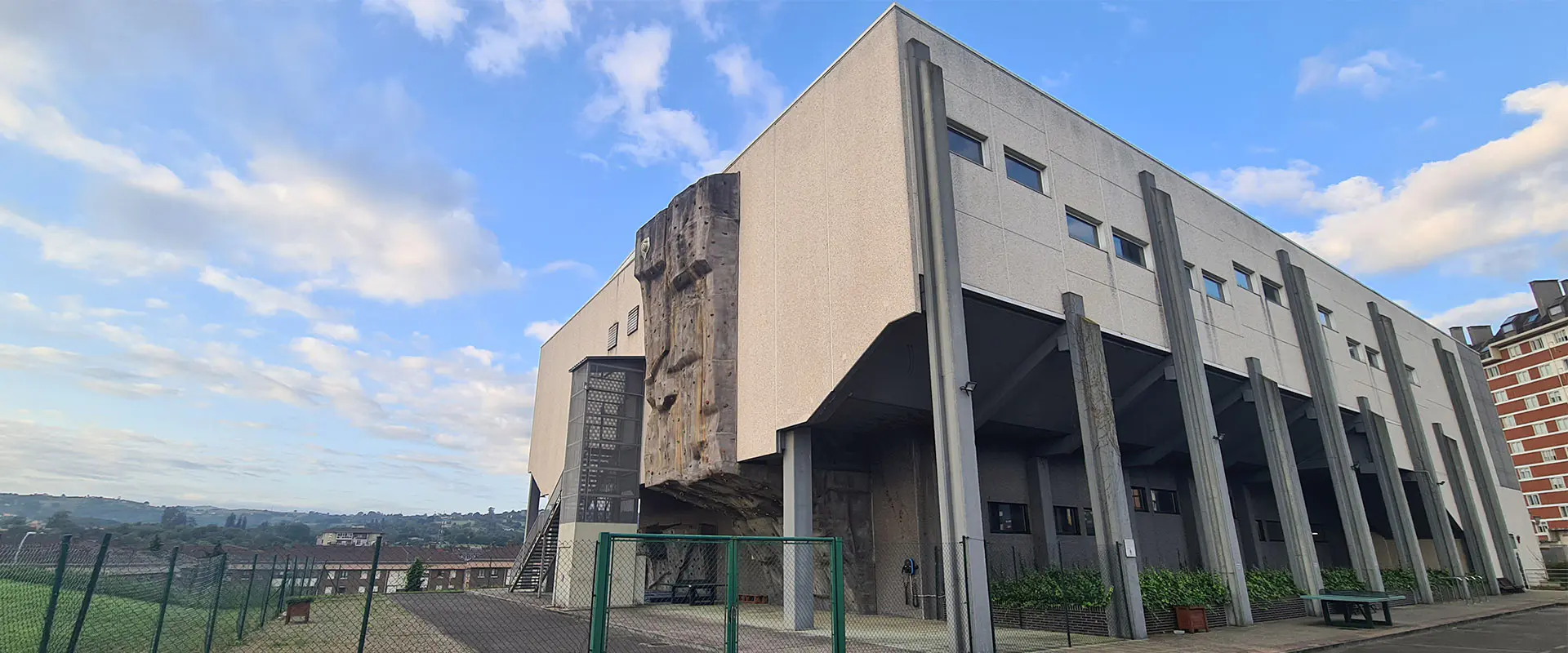 Vista lateral del exterior del edificio, con pasillo abovedado bajo sus columnas y detalle del rocódromo
