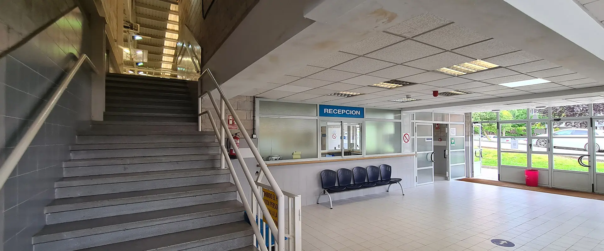 Interior de la recepción con escaleras a la izquierda, a la derecha hay un mostrador señalado con cartel azul de recepción