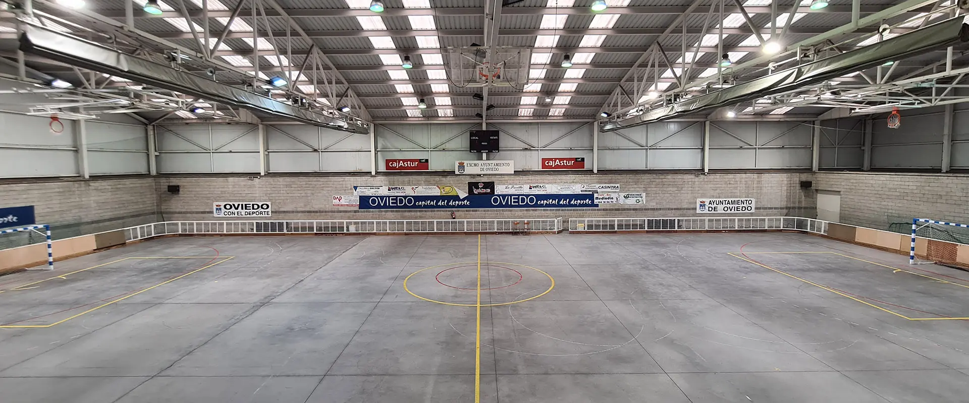 Pista polideportiva de hormigón pulido vista desde el centro y grada superior. Hay porterías a izquierda y derecha y canastas