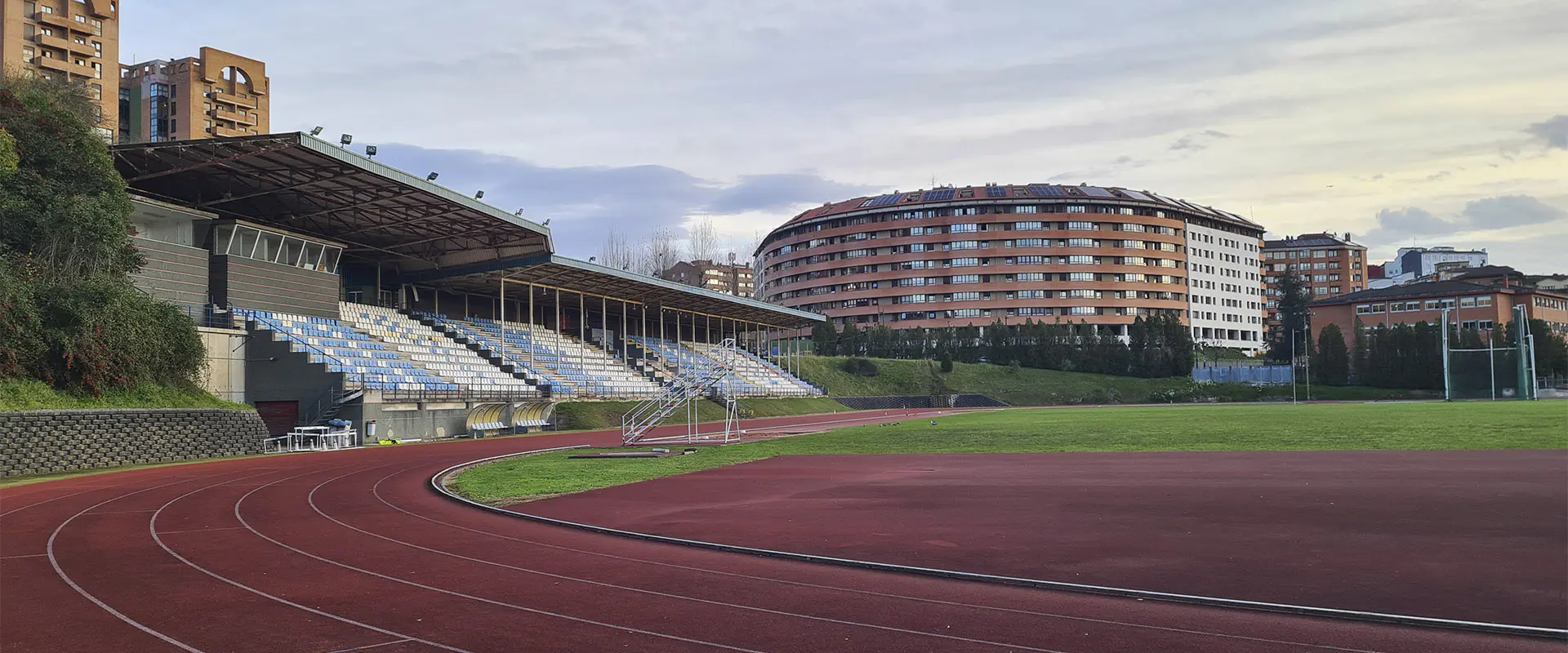 Vista lateral de las pistas de atletismo, con las gradas y edificios circundantes al fondo