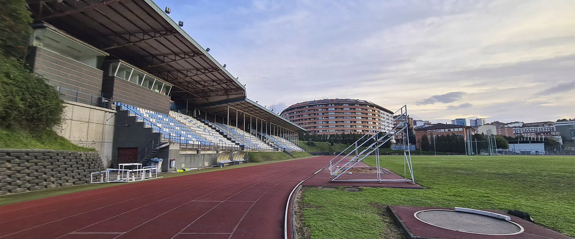 Vista de las pistas de atletismo, con las gradas en un lateral y detalle de la zona de lanzamiento de peso