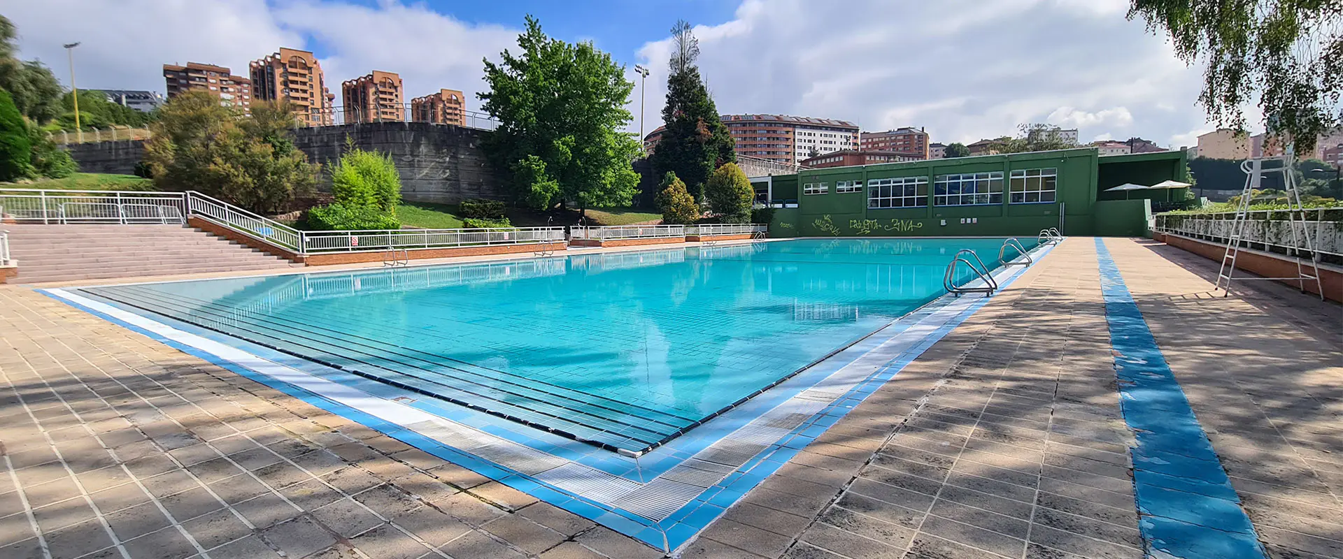 Vista de la piscina principal. Al fondo, edificio de instalaciones y edificios circundantes