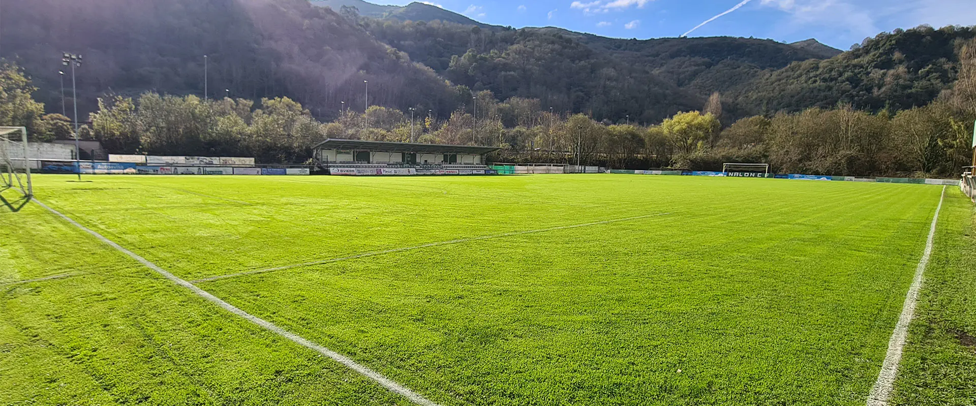 Terreno de juego a pie de campo y desde un córner, con las gradas al fondo y un entorno de árboles y montañas