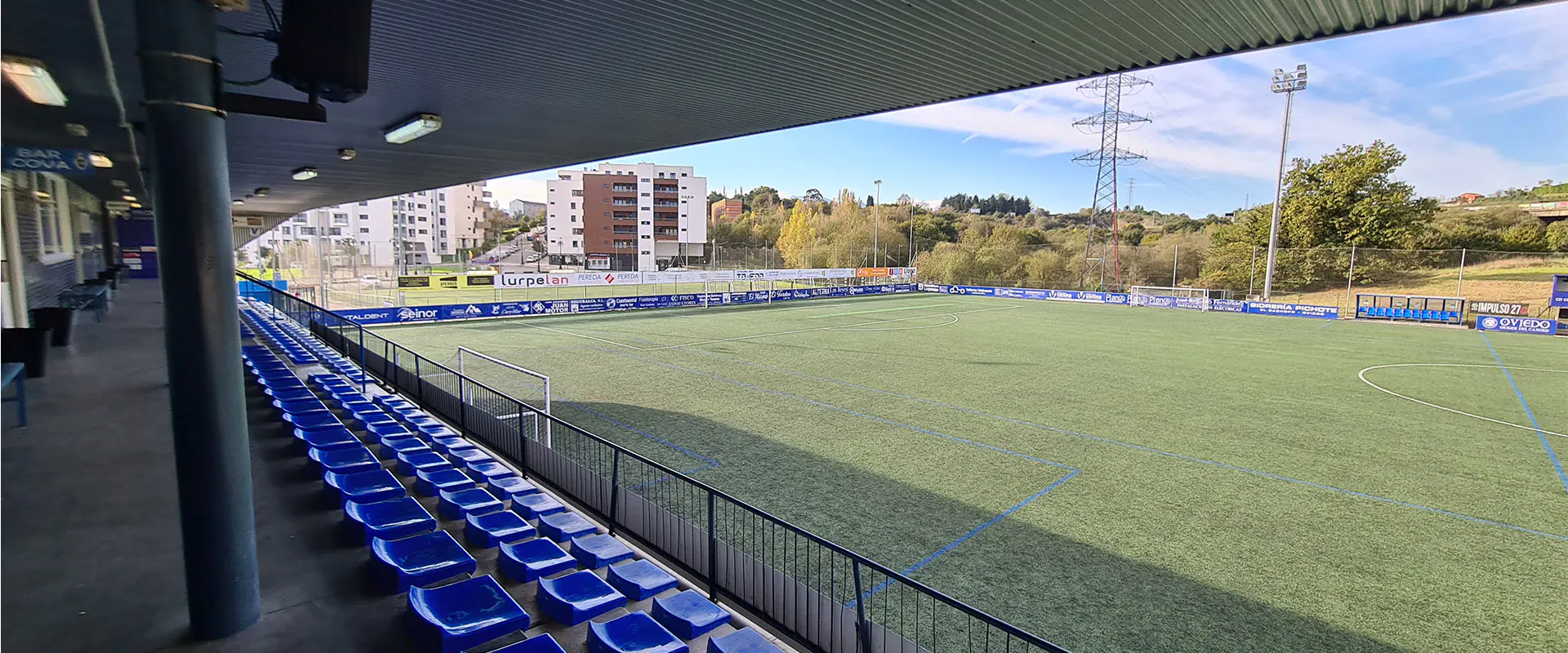 Vista lateral del campo desde el pasillo superior de las gradas, con las torres de iluminación y edificios al fondo