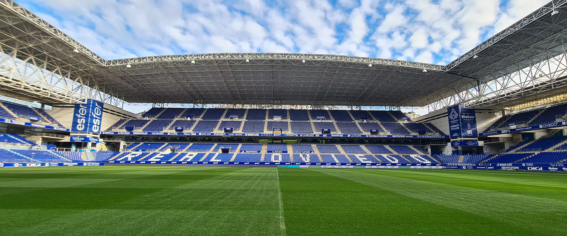 Vista a pie de campo de una tribuna lateral. Gradas con letras blancas en sus bancos que forman las palabras Real Oviedo