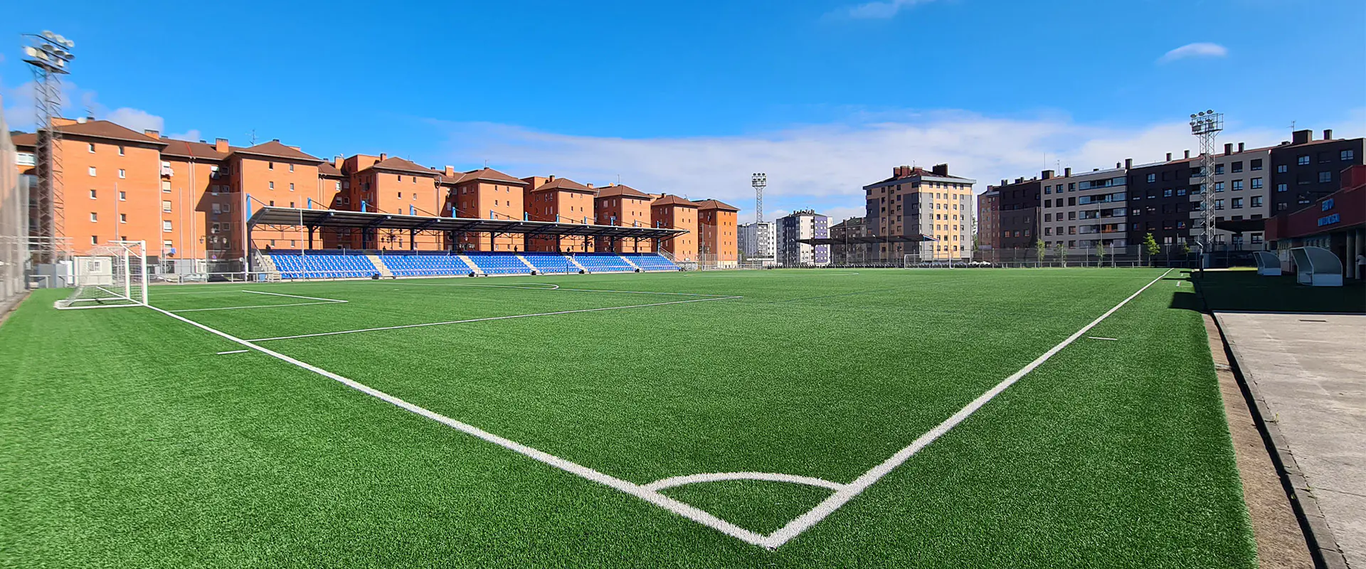 Terreno de juego a pie de campo desde un córner. Gradas en un lateral y edificios al fondo
