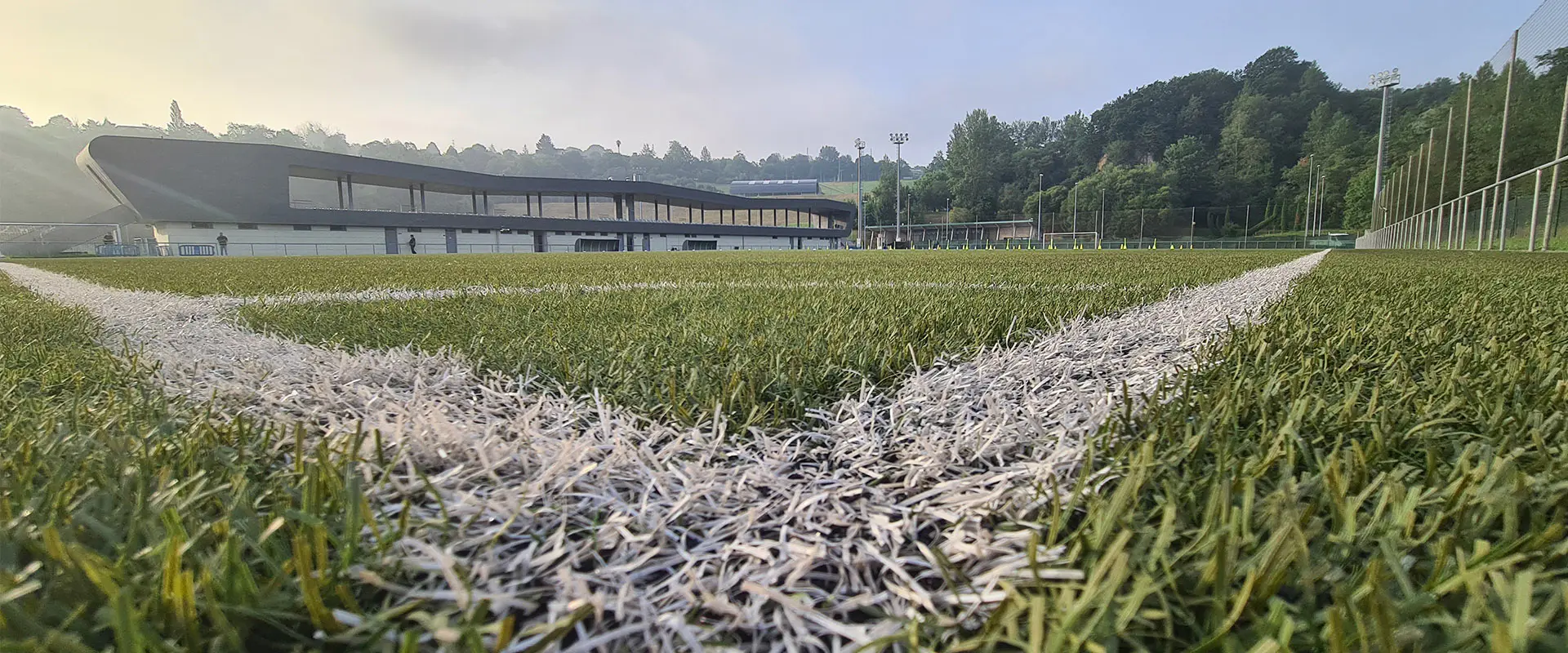Vista a ras de suelo desde uno de los córneres de un campo de fútbol 11, con las gradas al fondo