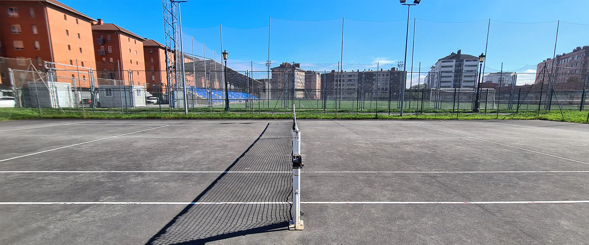 Pista de tenis desde un lateral, con la red en el centro. Estadio Manuel Díaz Vega al fondo