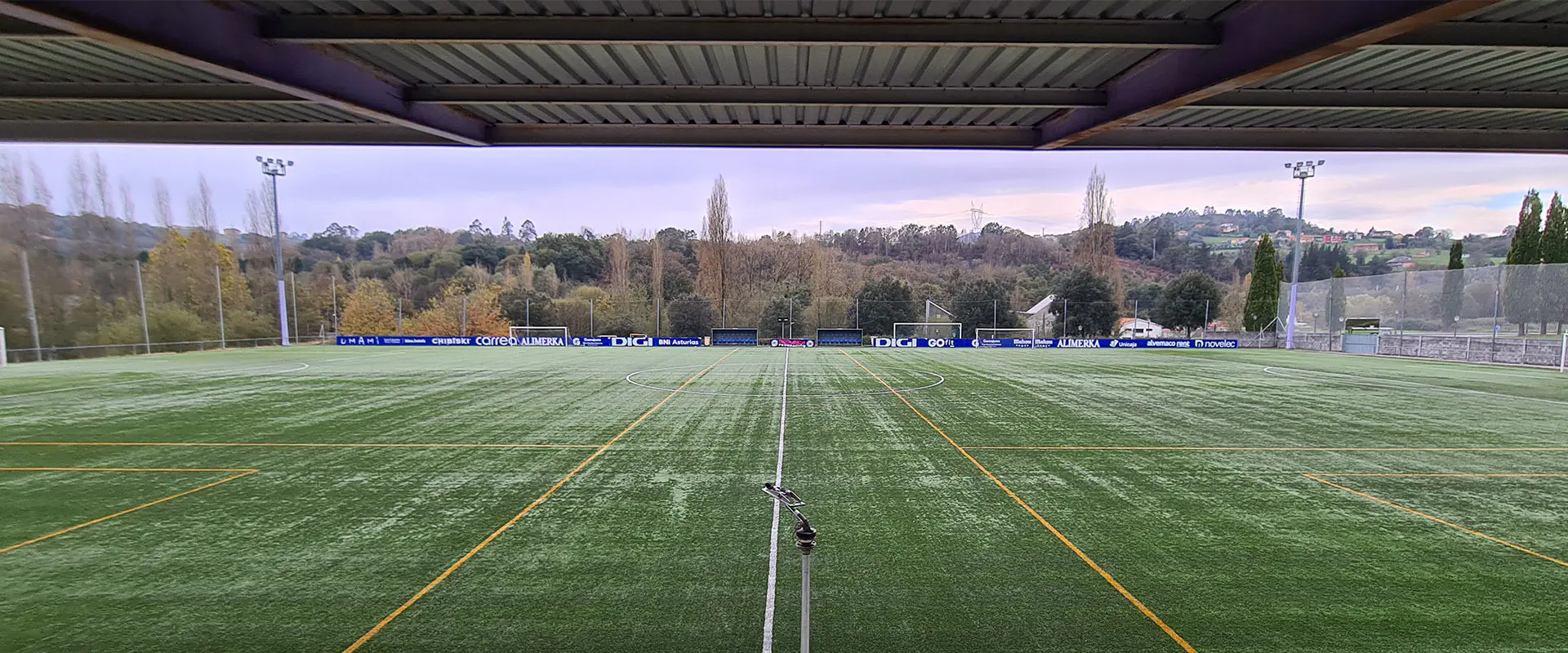 Terreno de juego desde las gradas. Vallas publicitarias al fondo. Detalle de la cubierta de las gradas en primer plano