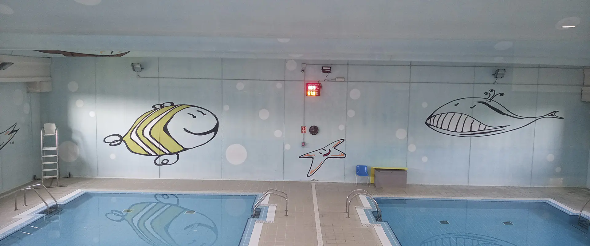 Vista de las dos piscinas de aprendizaje, con el pasillo divisor y pinturas de peces, de carácter infantil, en las paredes