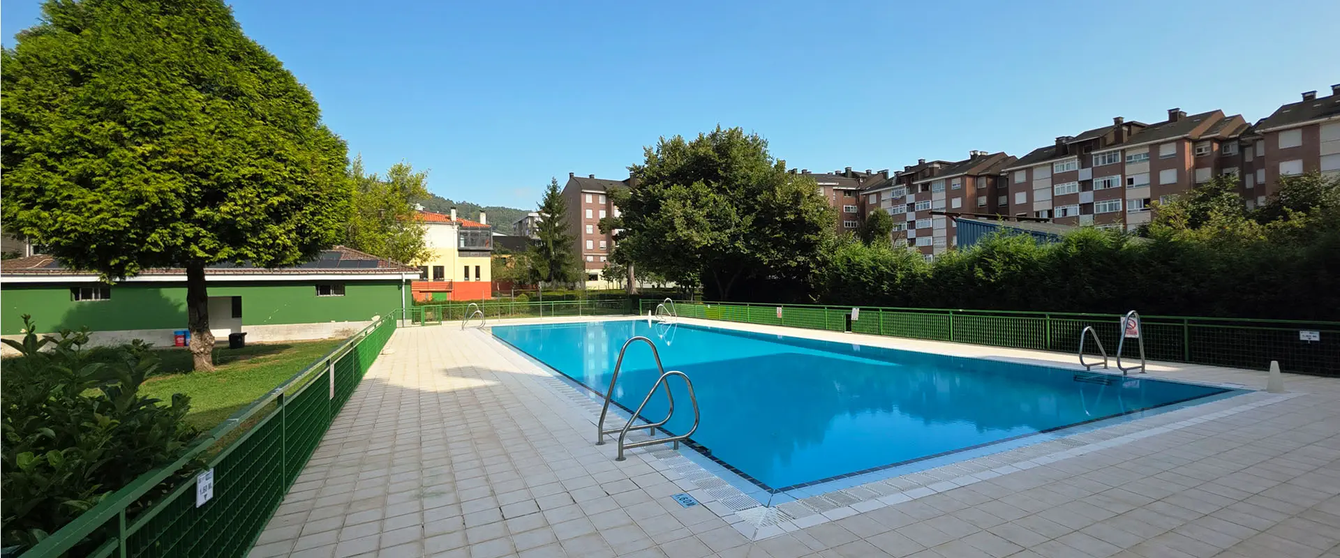vista de la piscina desde una esquina con el edificio de servicios al fondo