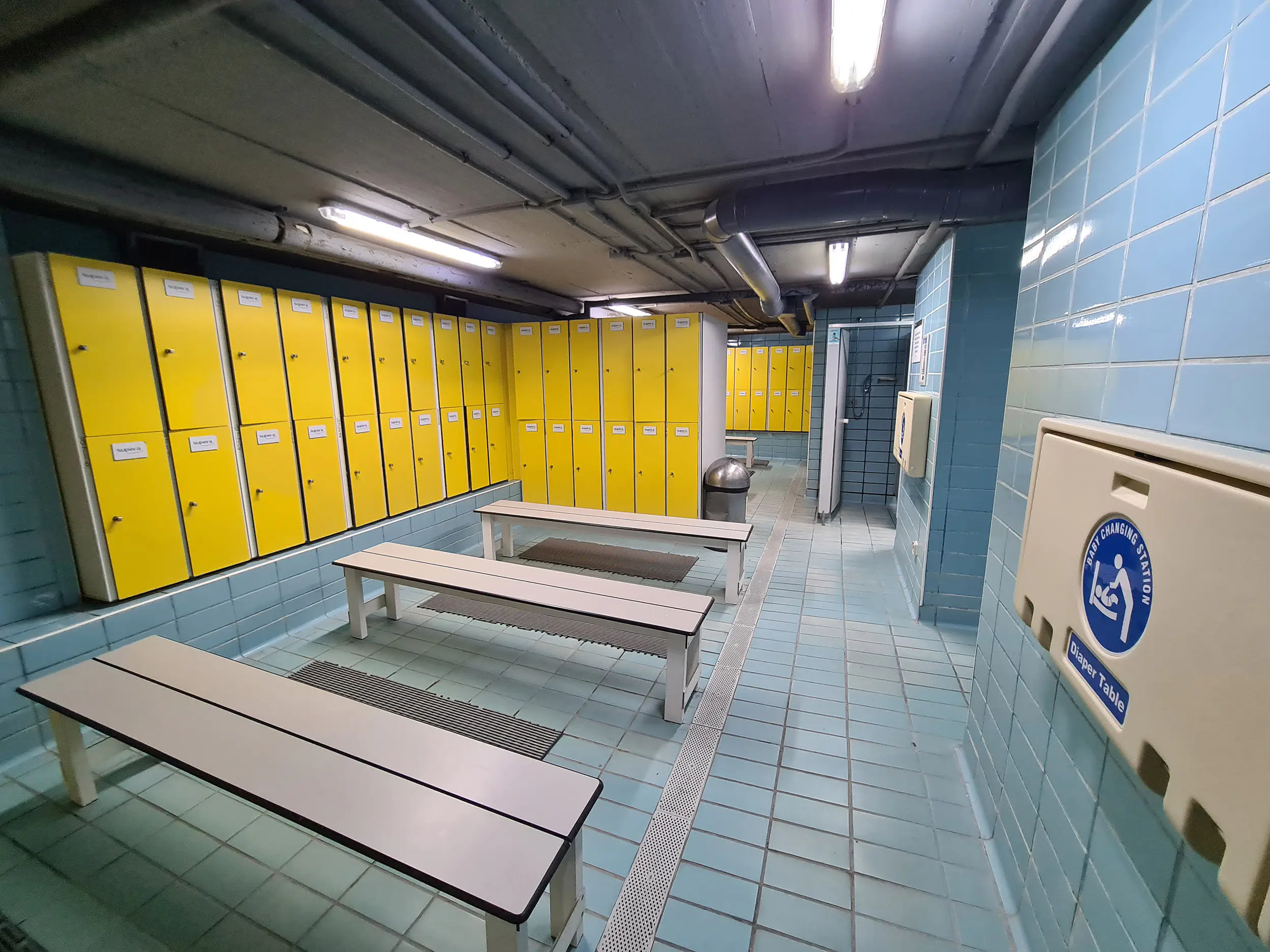 Interior de los vestuarios, con bancos, taquillas y cambiador de pañales horizontal plegable