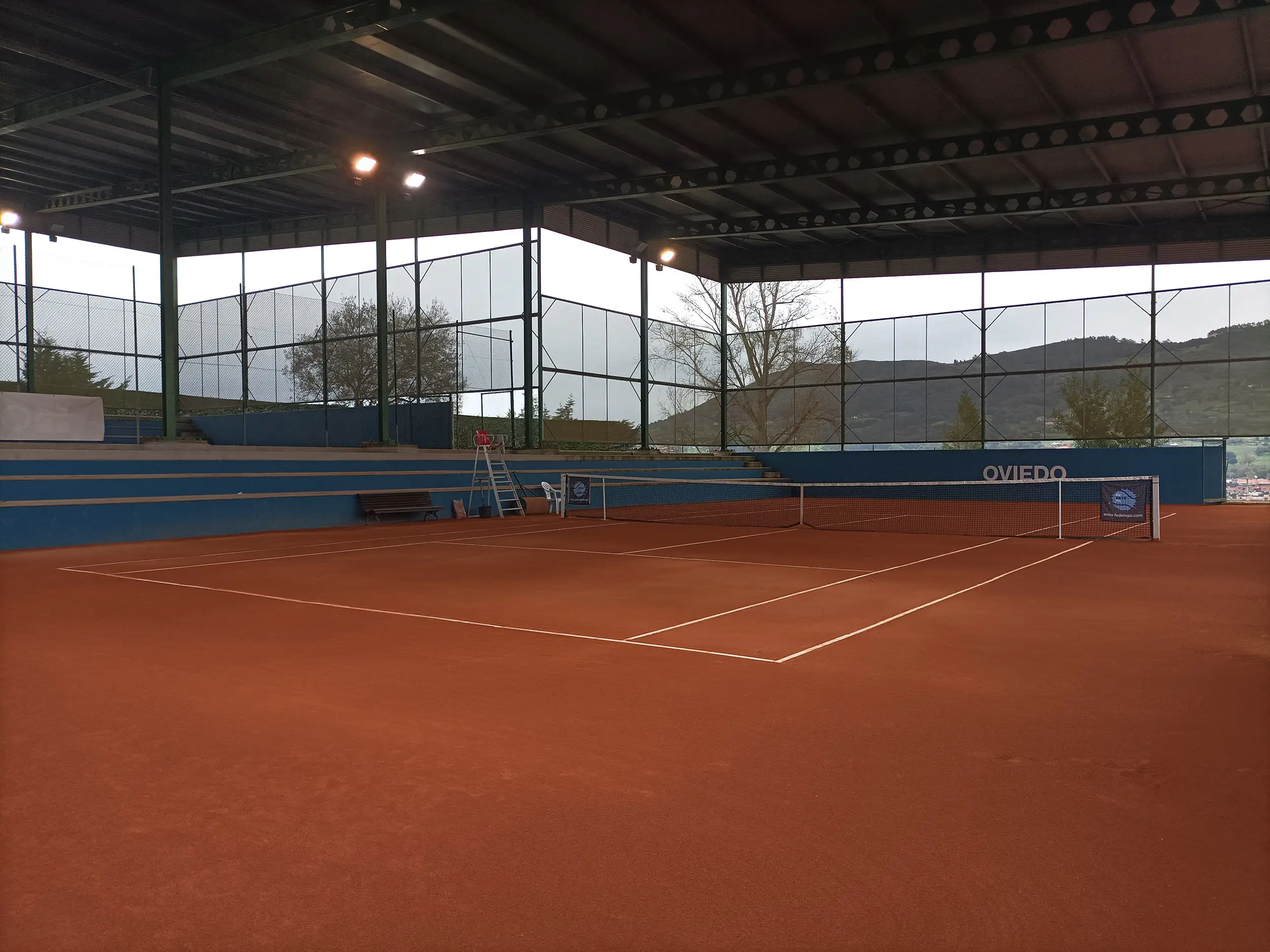 Vista general de una pista de tenis de tierra batida cubierta, con las gradas laterales y la cubierta
