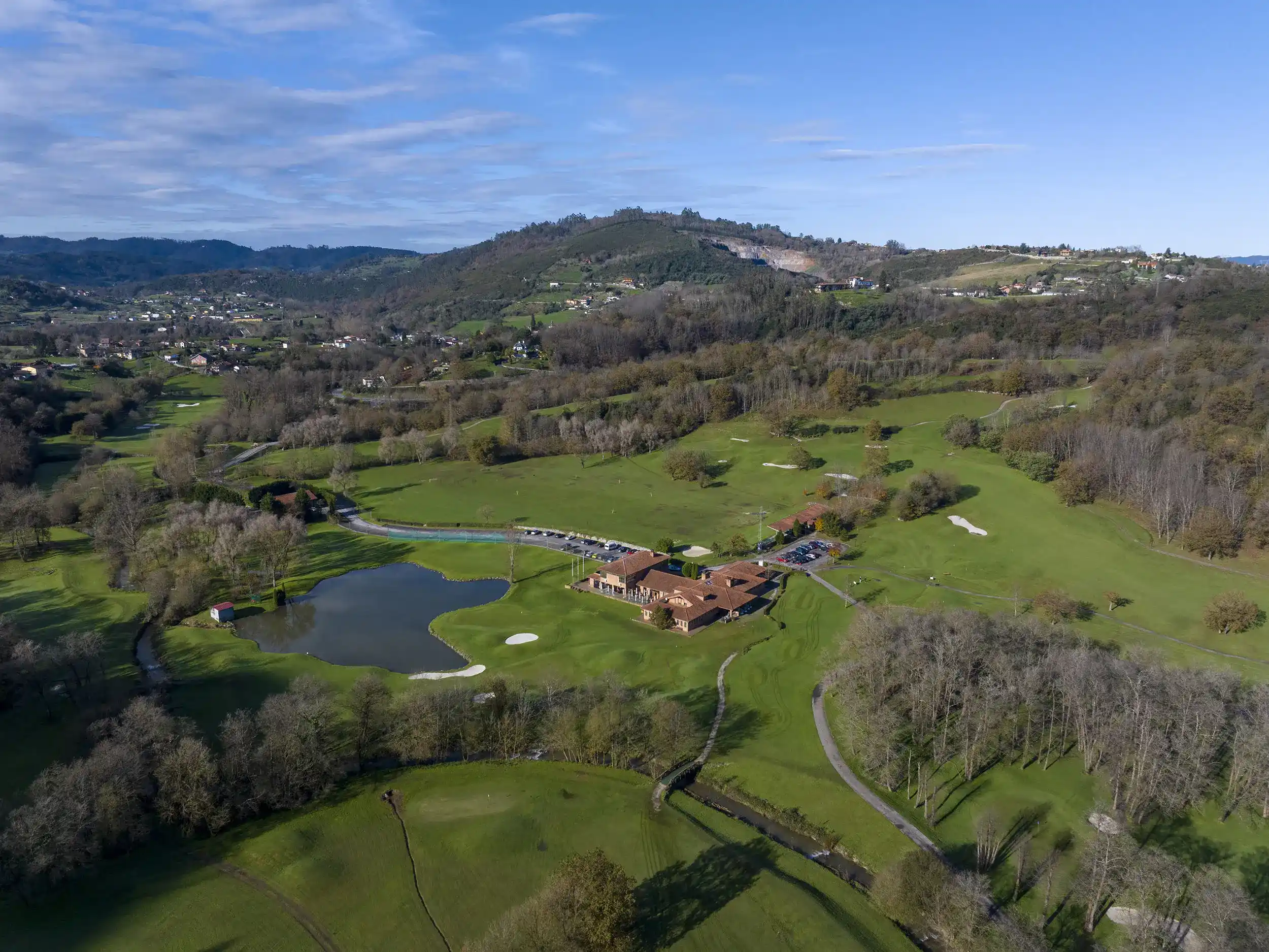 Vista aérea del campo de golf de Las Caldas, con grandes áreas verdes circundantes y un pequeño lago