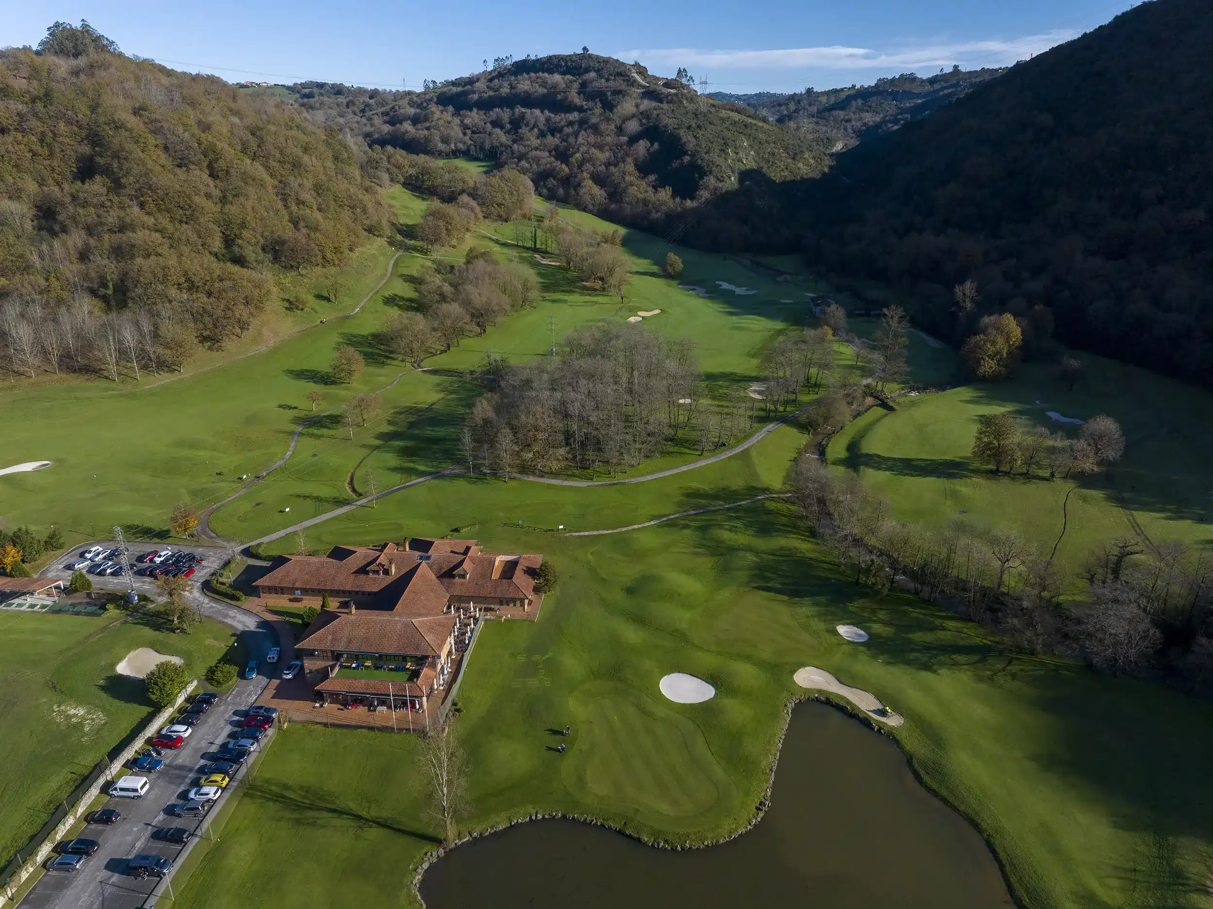 Vista aérea del edificio principal, aparcamiento anexo, un pequeño lago y primeros hoyos del recorrido del campo