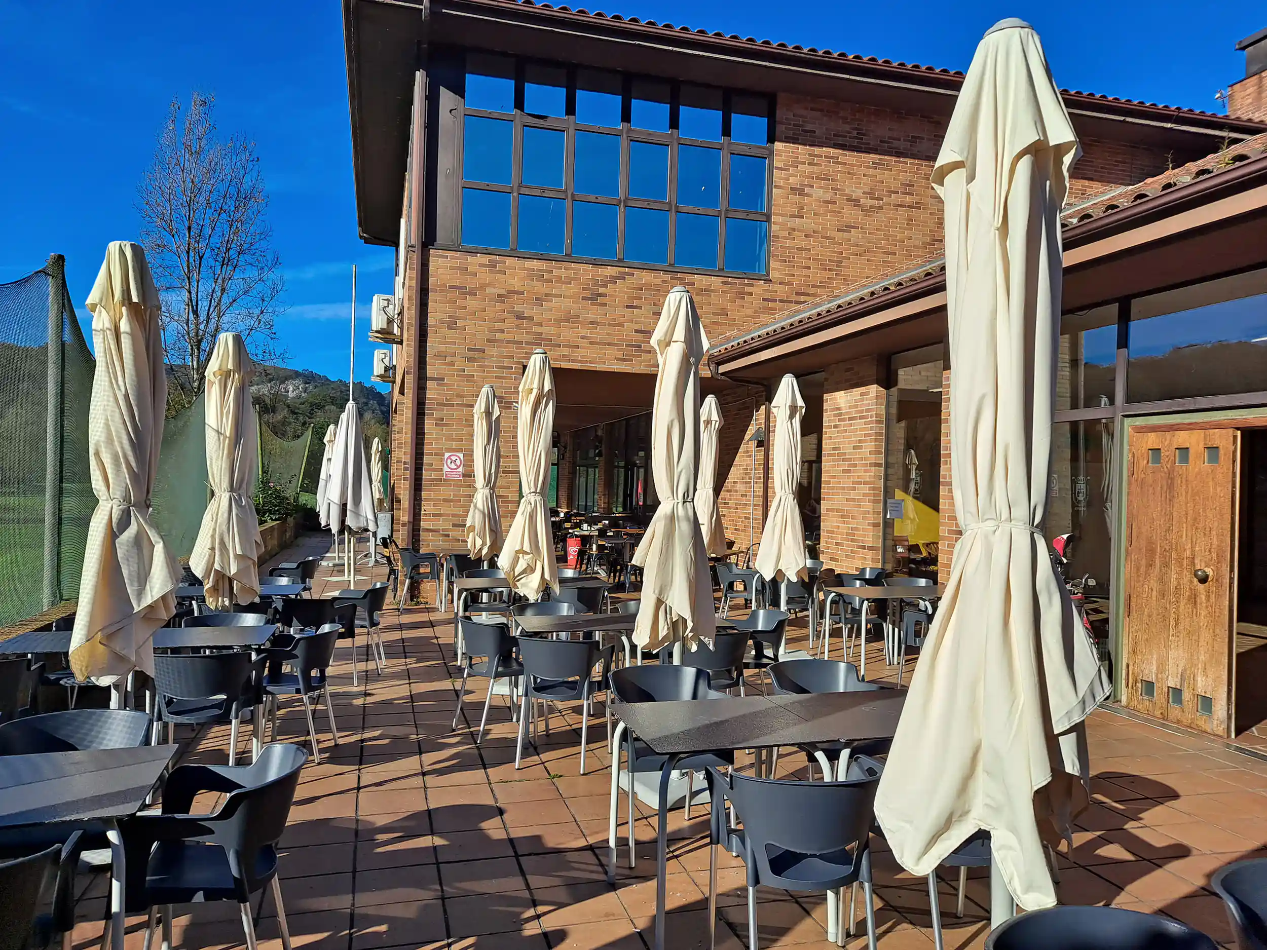 Terraza exterior del restaurante-cafetería, con mesas, sillas y sombrillas plegadas
