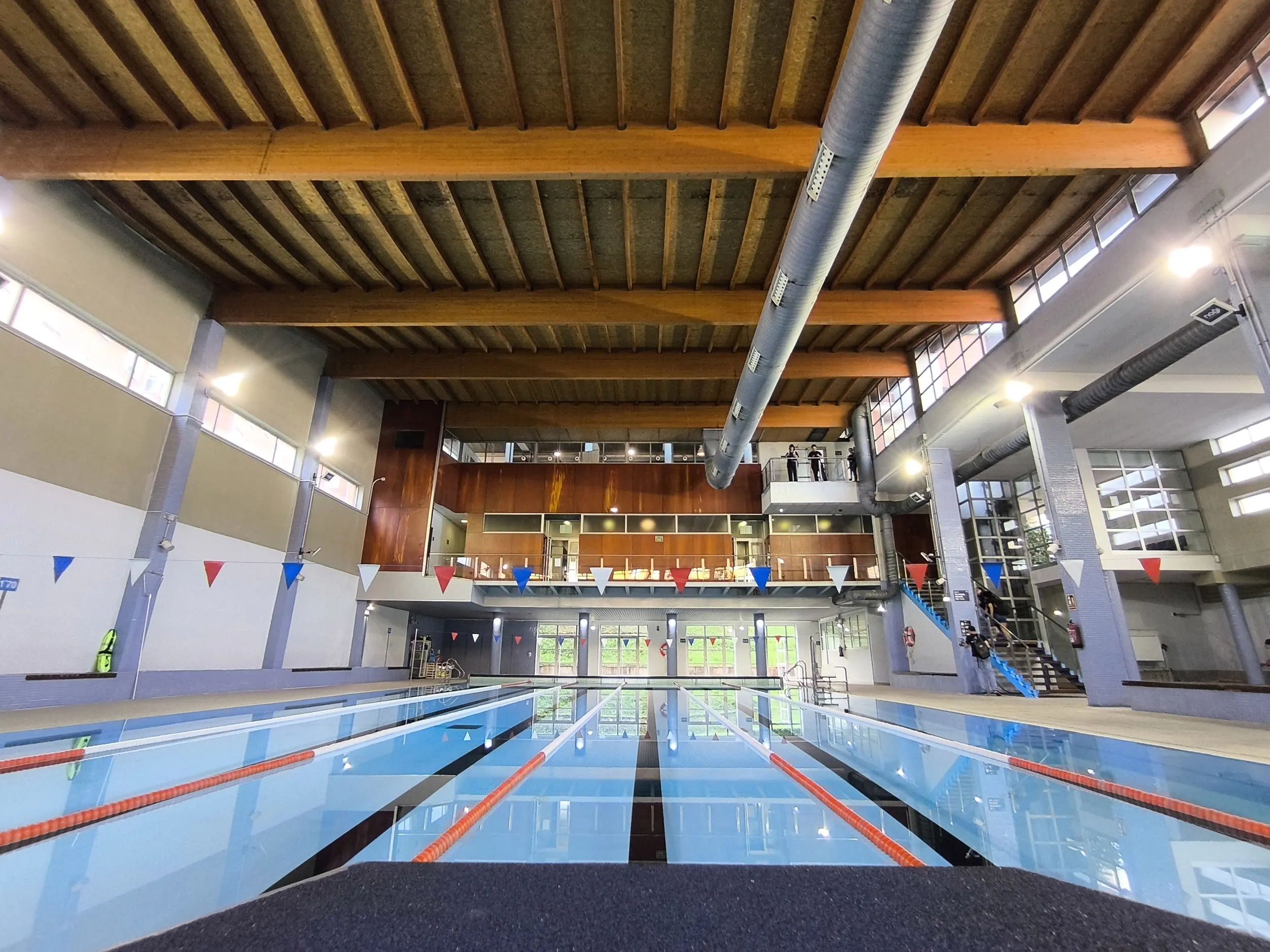 Vista a ras de suelo de la piscina climatizada, con detalle de la cubierta de madera y vista al fondo del piso superior