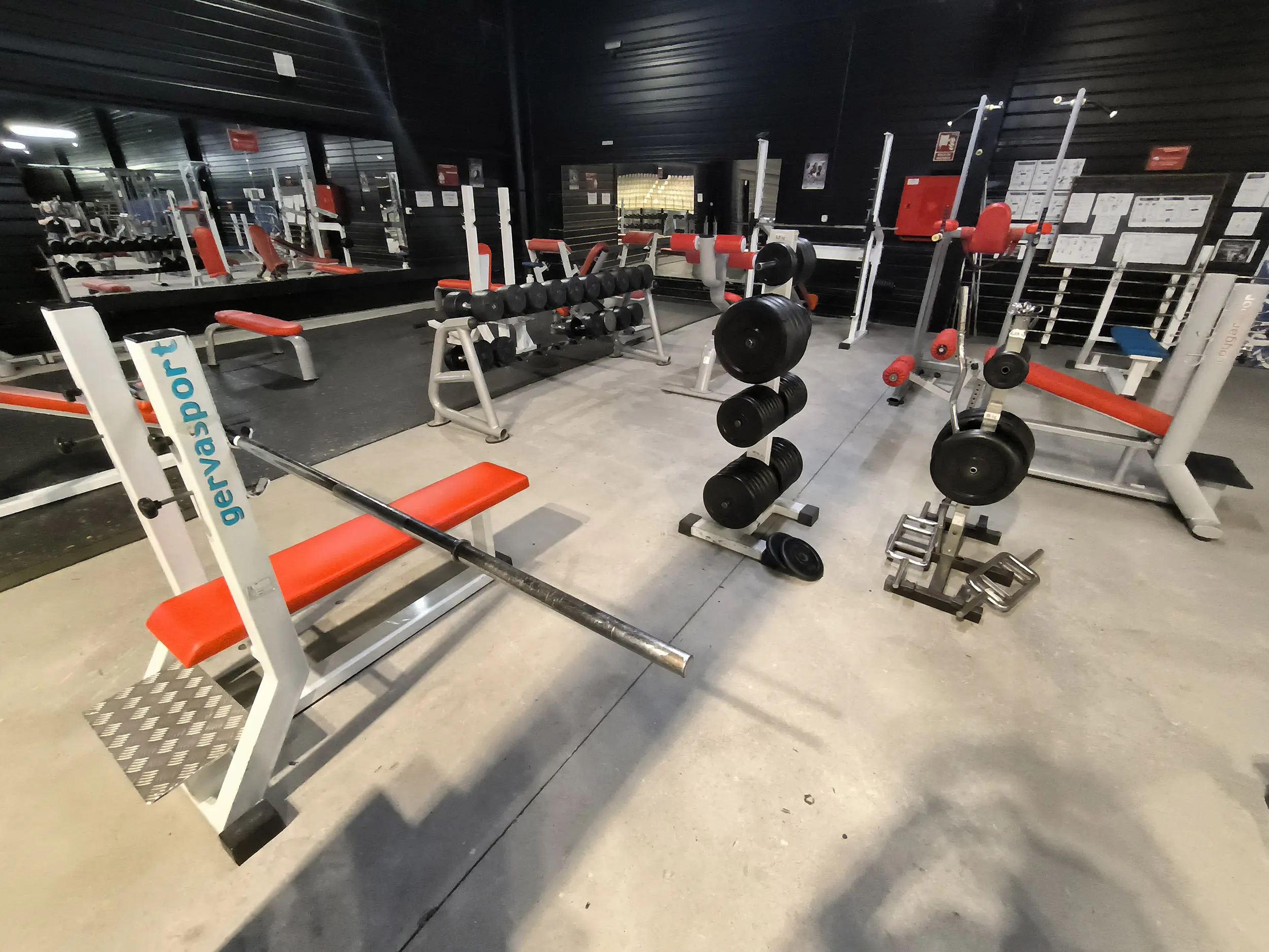 Detalle de la sala polivalente 2, con espejo en un lateral, bancos de gimnasia, pesas y  máquinas de musculación