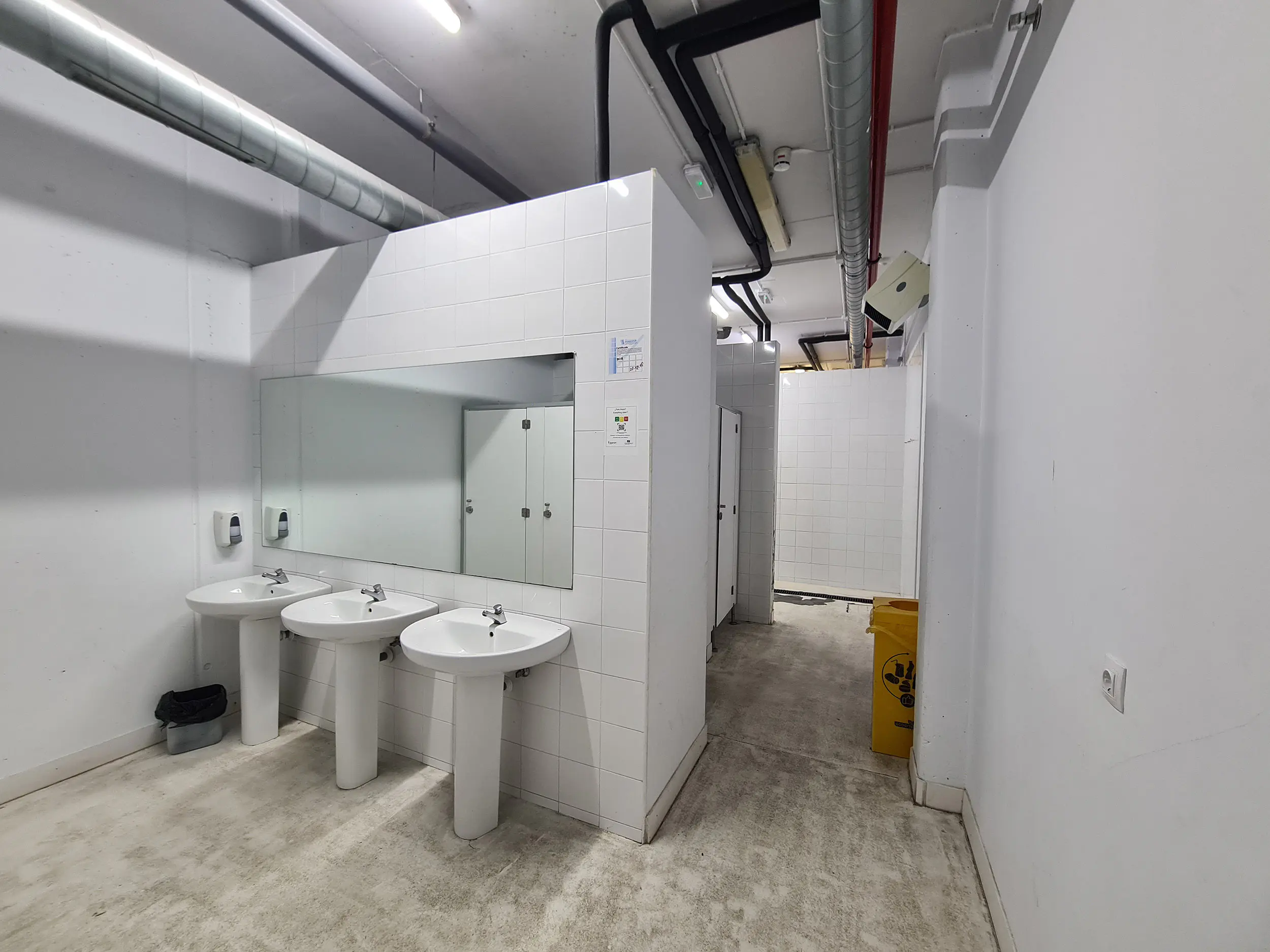 Zona de aseos de los vestuarios, con lavabos, espejo frontal y pasillo de acceso