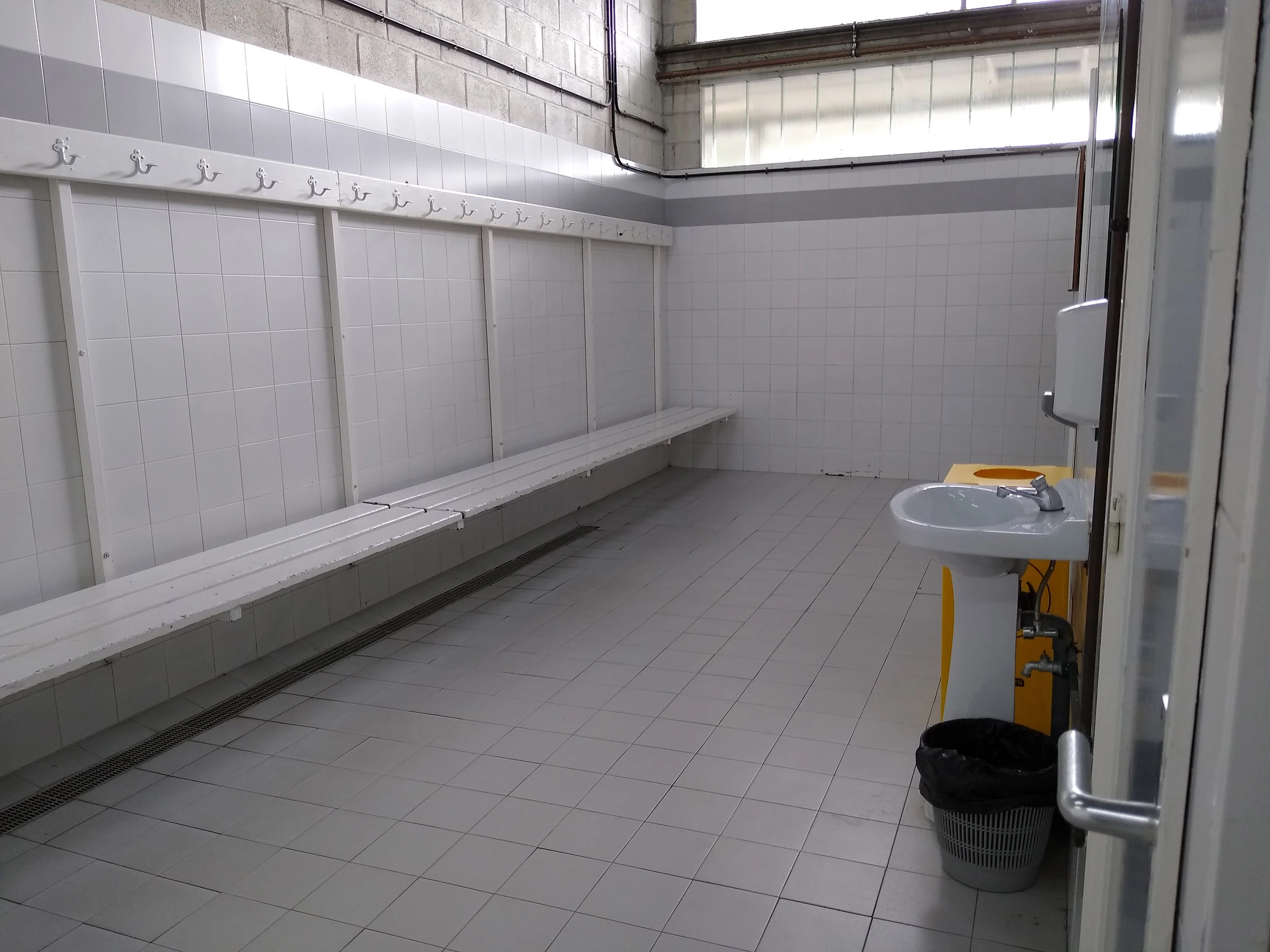 Interior de uno de los vestuarios. Lavabo y fila de bancos con perchas