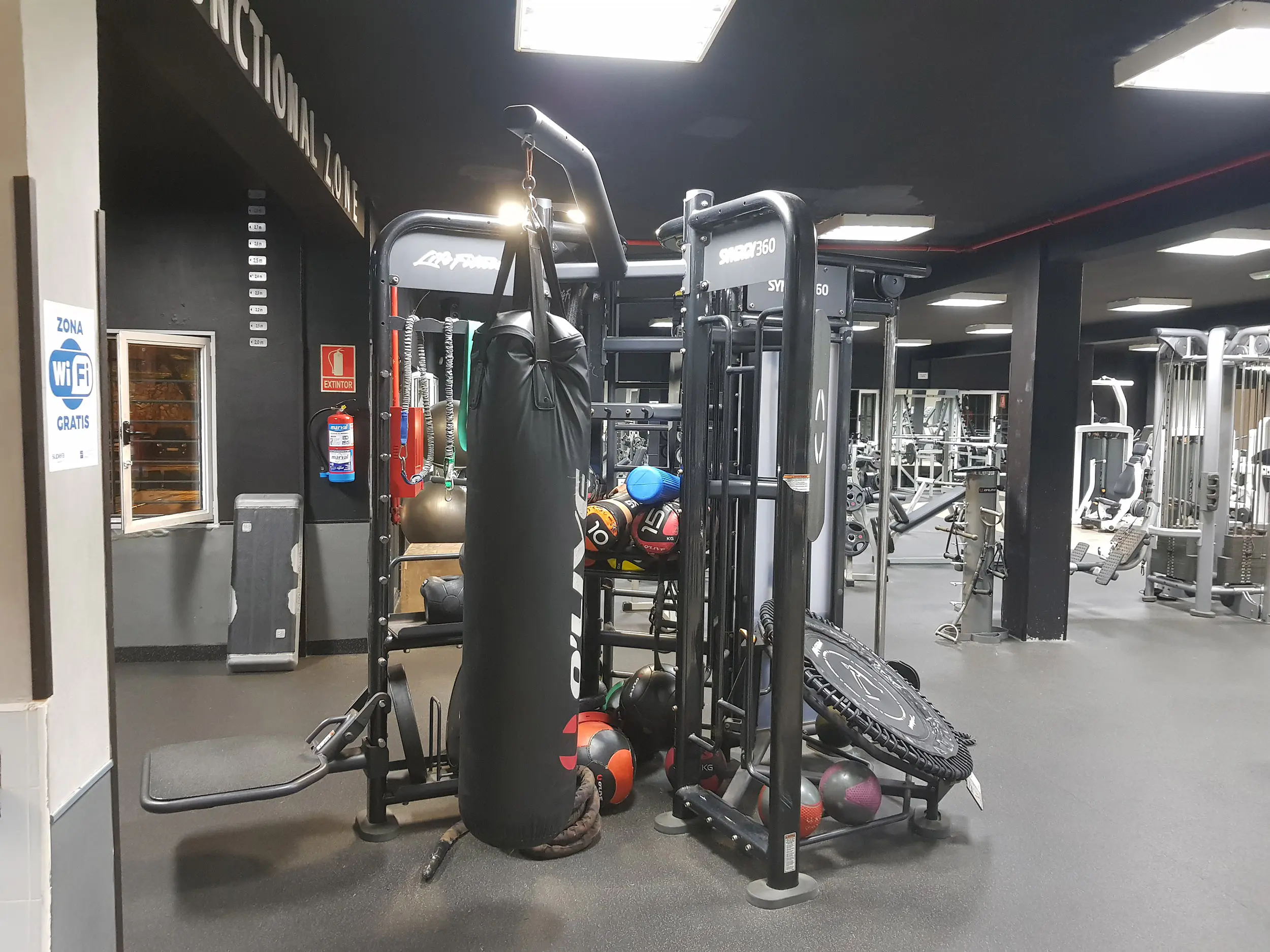 Sala de musculación, con máquina de musculación en primer plano y otras máquinas deportivas al fondo