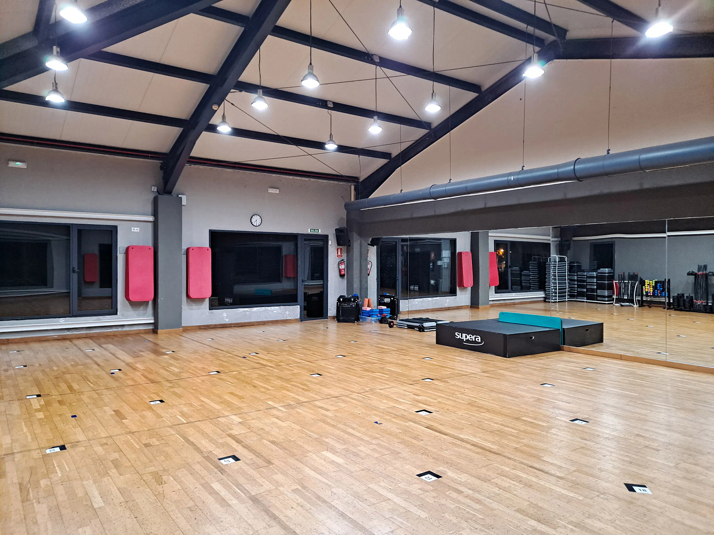 Vista en detalle de una zona de la sala polivalente, con un gran espejo y diversos accesorios deportivos