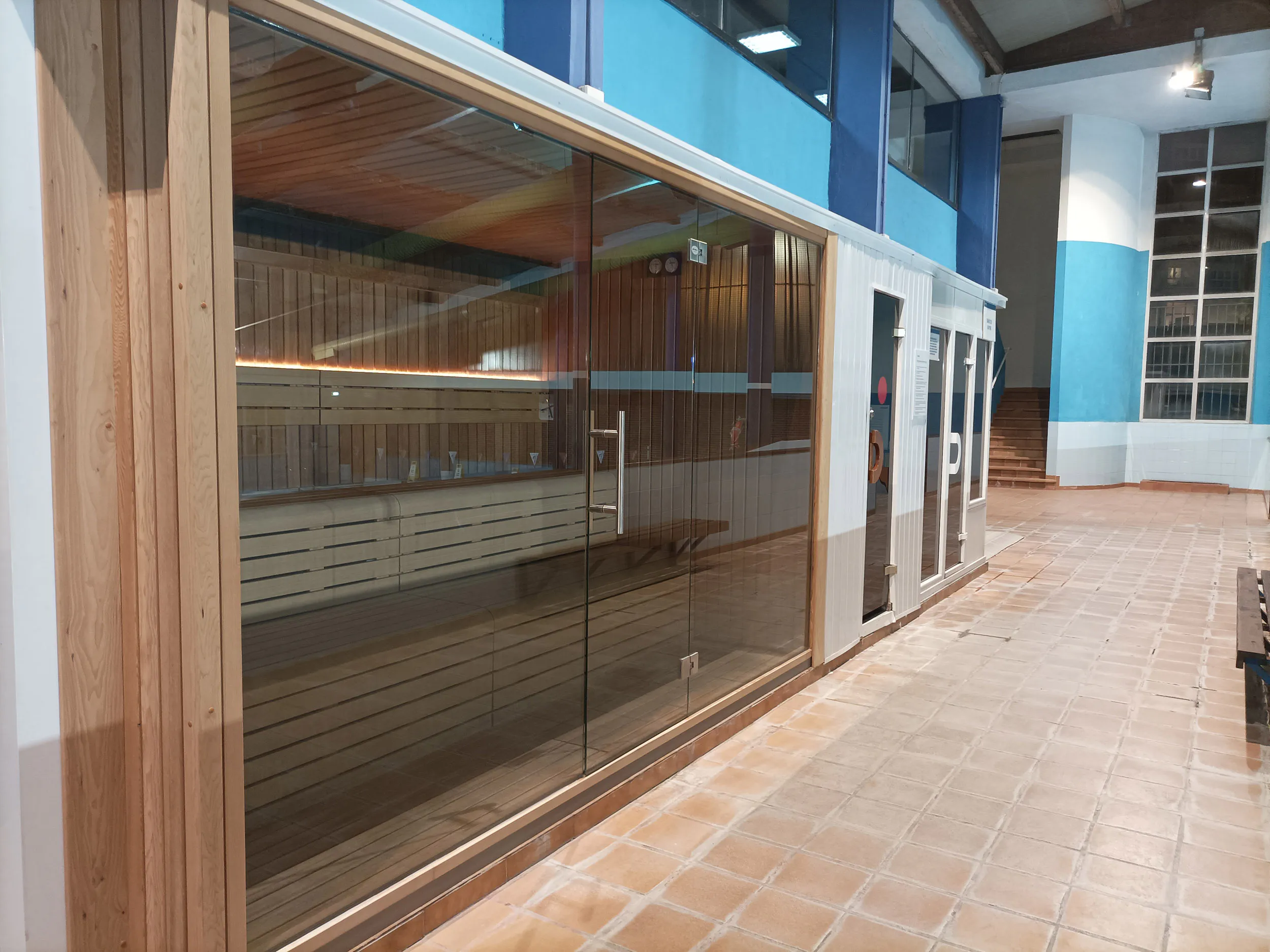 Sala de sauna, con vista lateral de los bancos de madera de su interior a través de la cristalera exterior