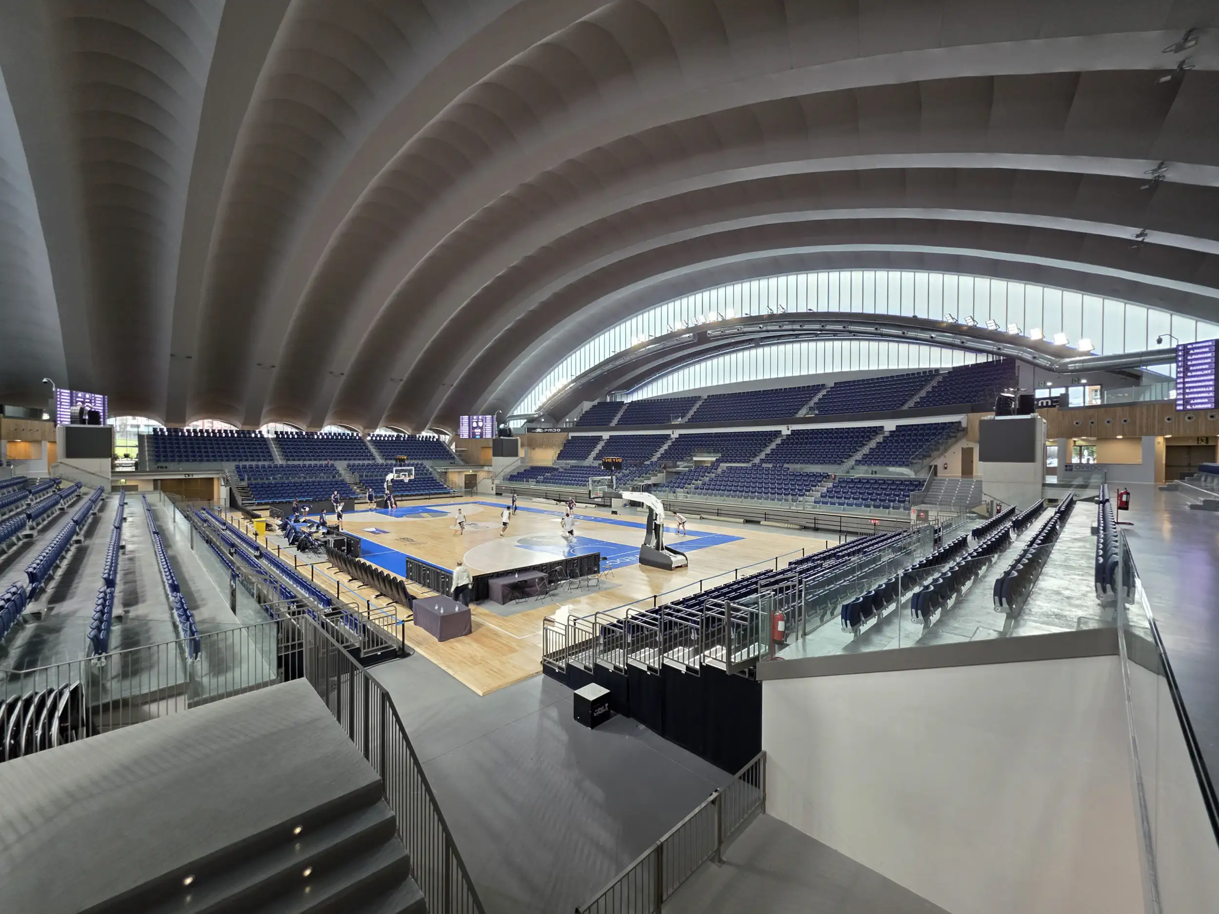 Vista interior desde una esquina con la pista de baloncesto y las gradas bajo la cubierta curva del recinto