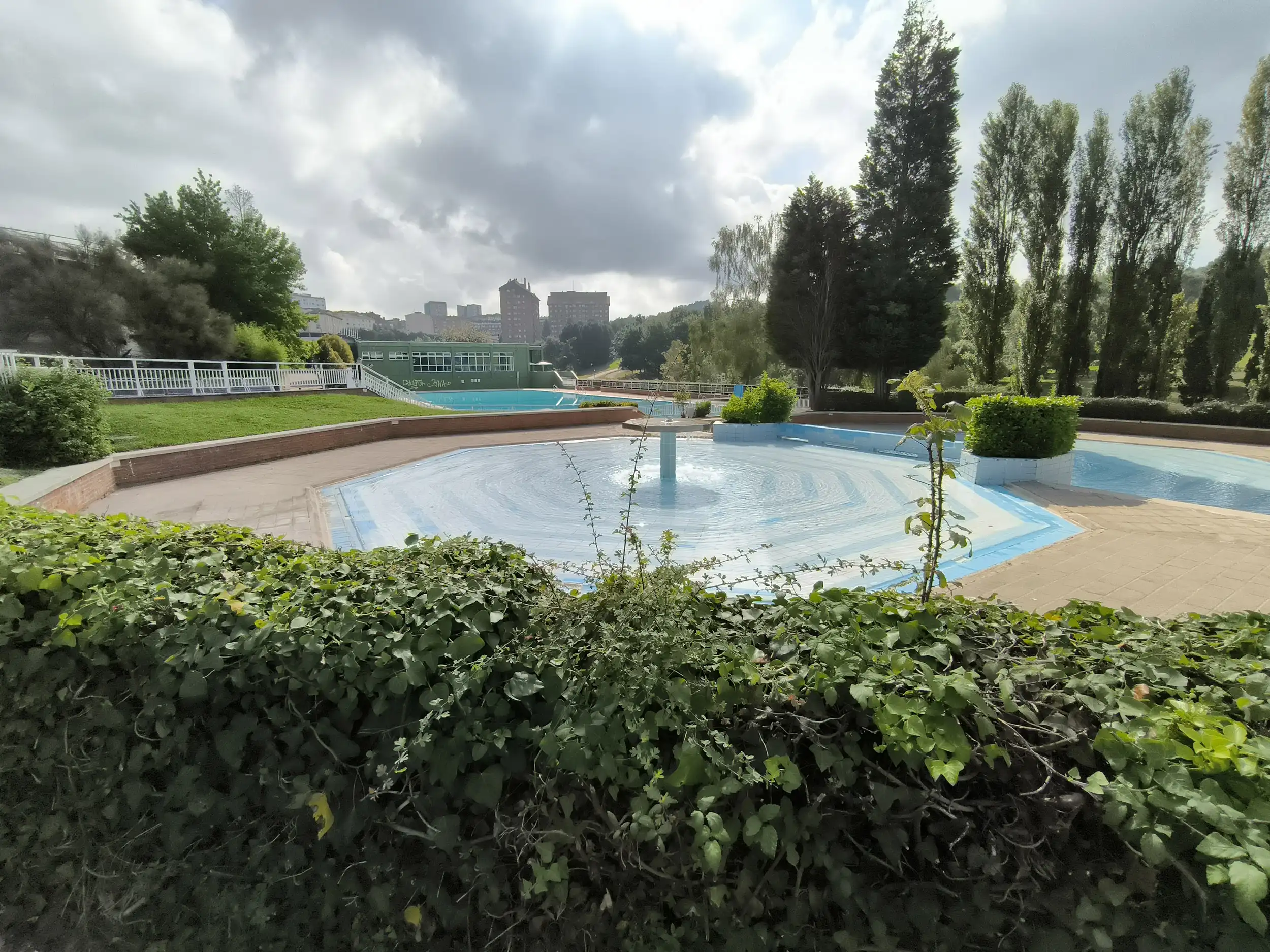 Piscina infantil con una fuente central interior y rodeada de jardines y árboles  