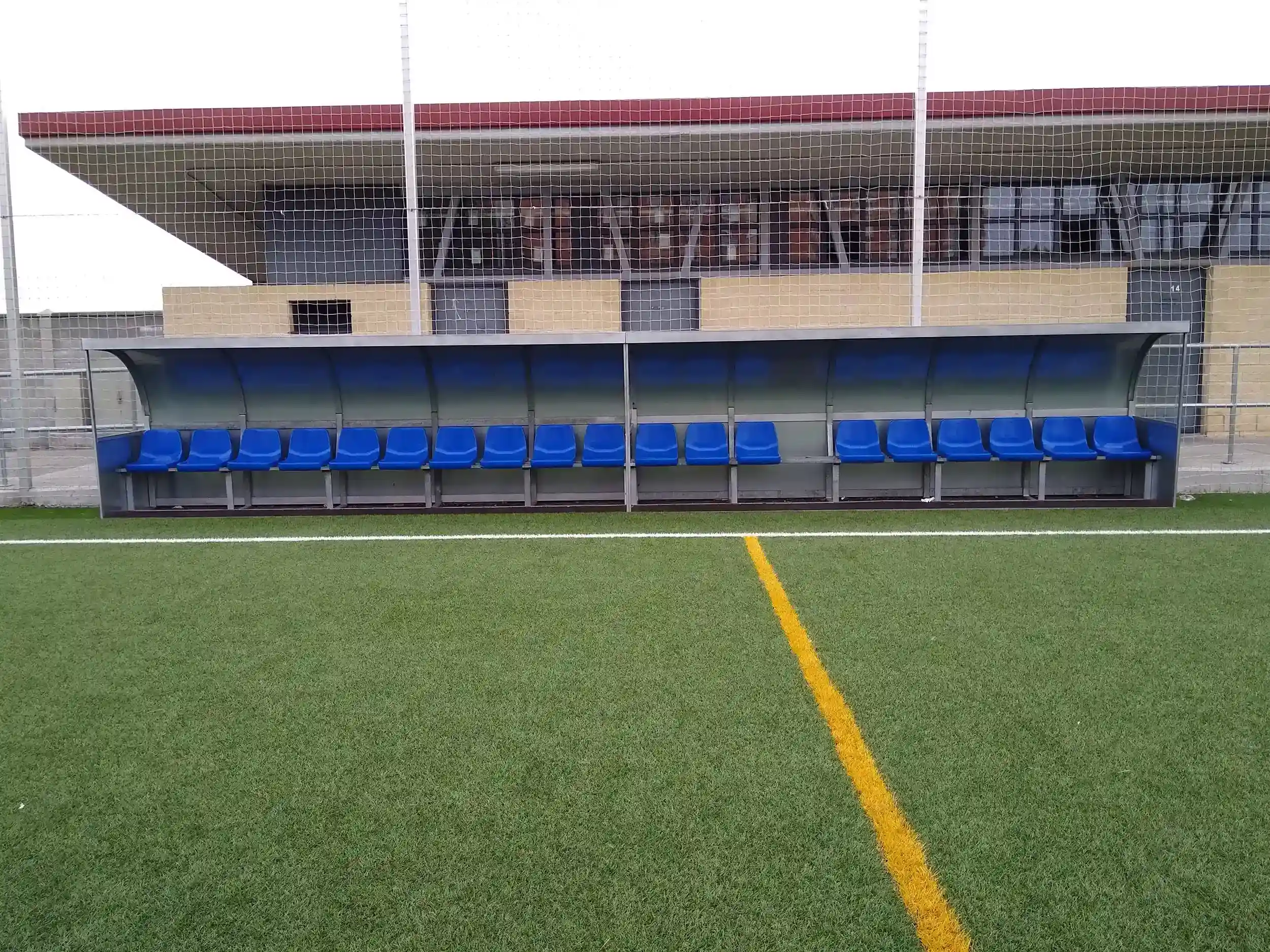 Vista de frente del  banquillo de suplentes y equipo técnico con cubierta metalizada y asientos azules