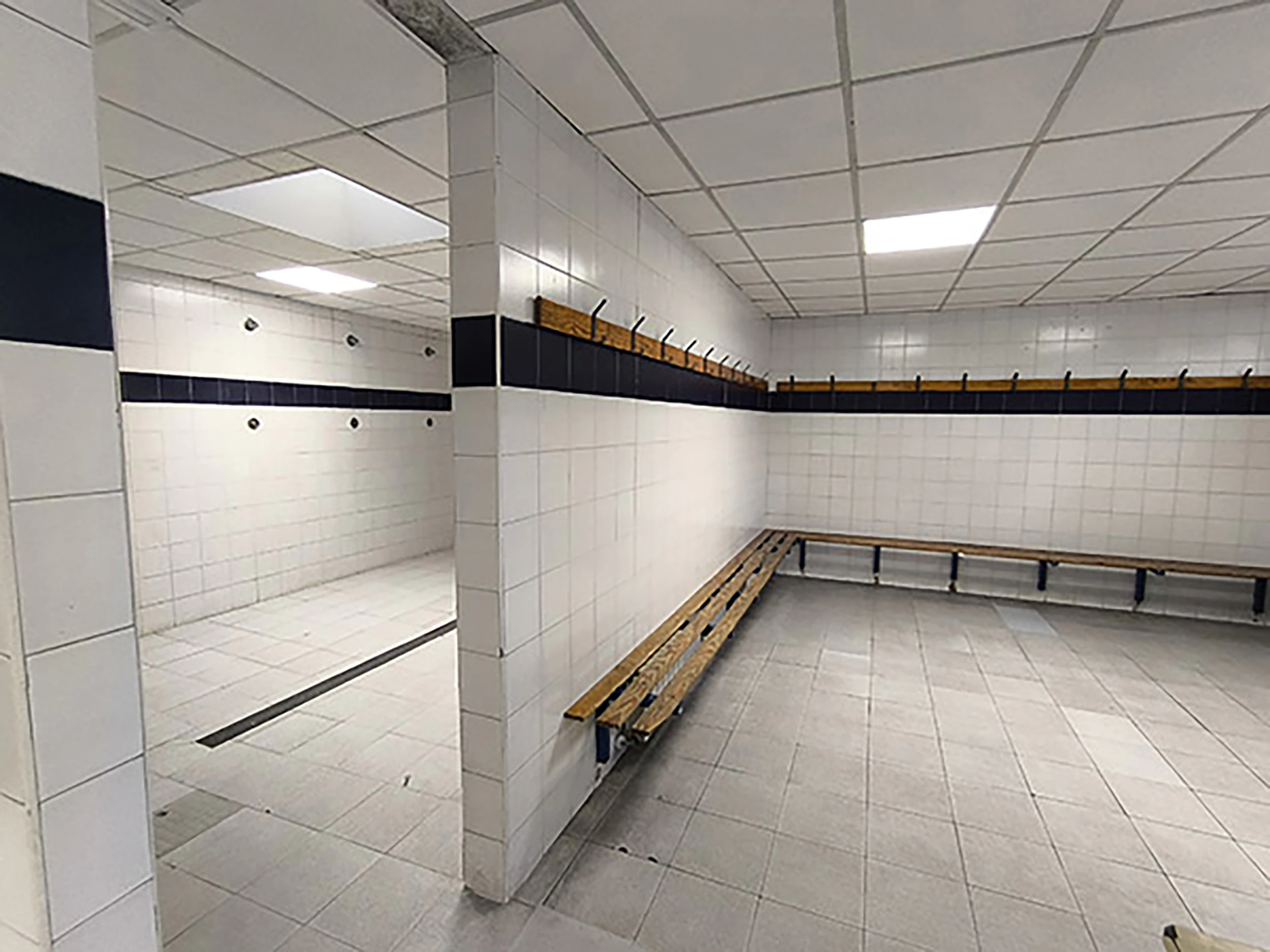 Interior de los vestuarios. A la izquierda, zona duchas y a la derecha, bancos y percheros de madera