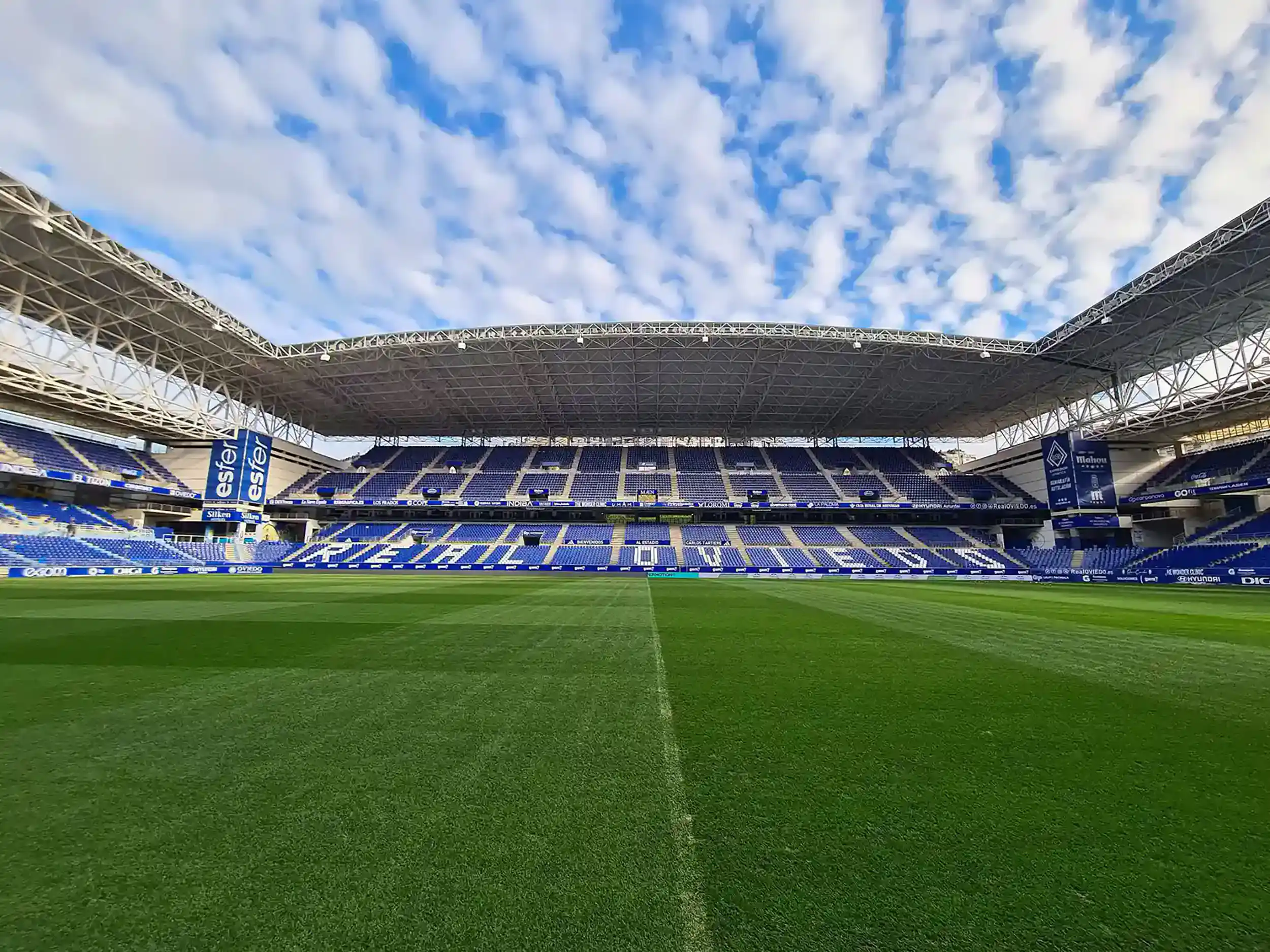 De frente y desde pie de campo tribuna techada con su diferentes niveles y en letras blancas: Real Oviedo