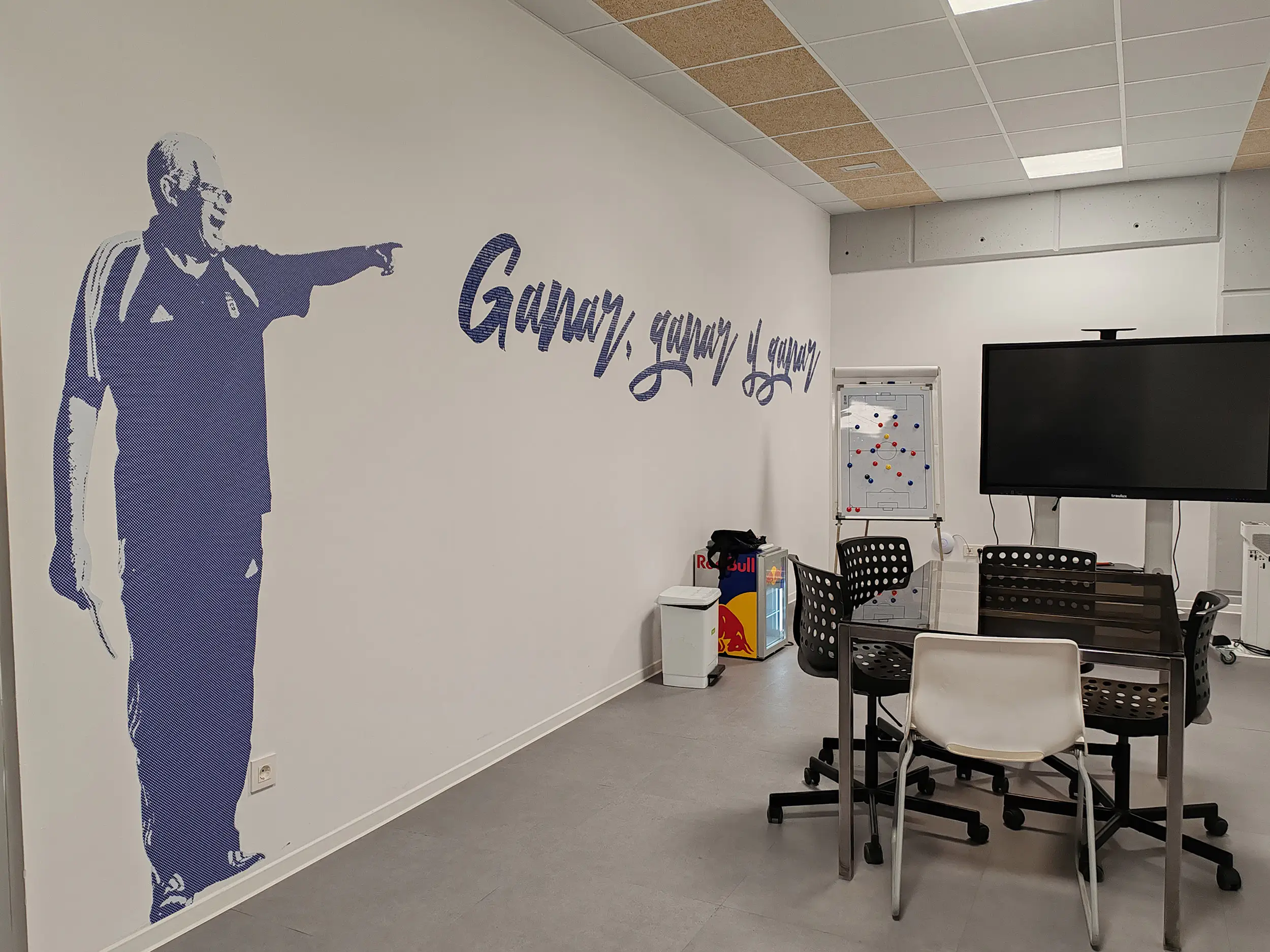 Sala técnica. Muro lateral decorado con imagen de Luis Aragonés de pie señalando y frase en azul: "Ganar, ganar y ganar"