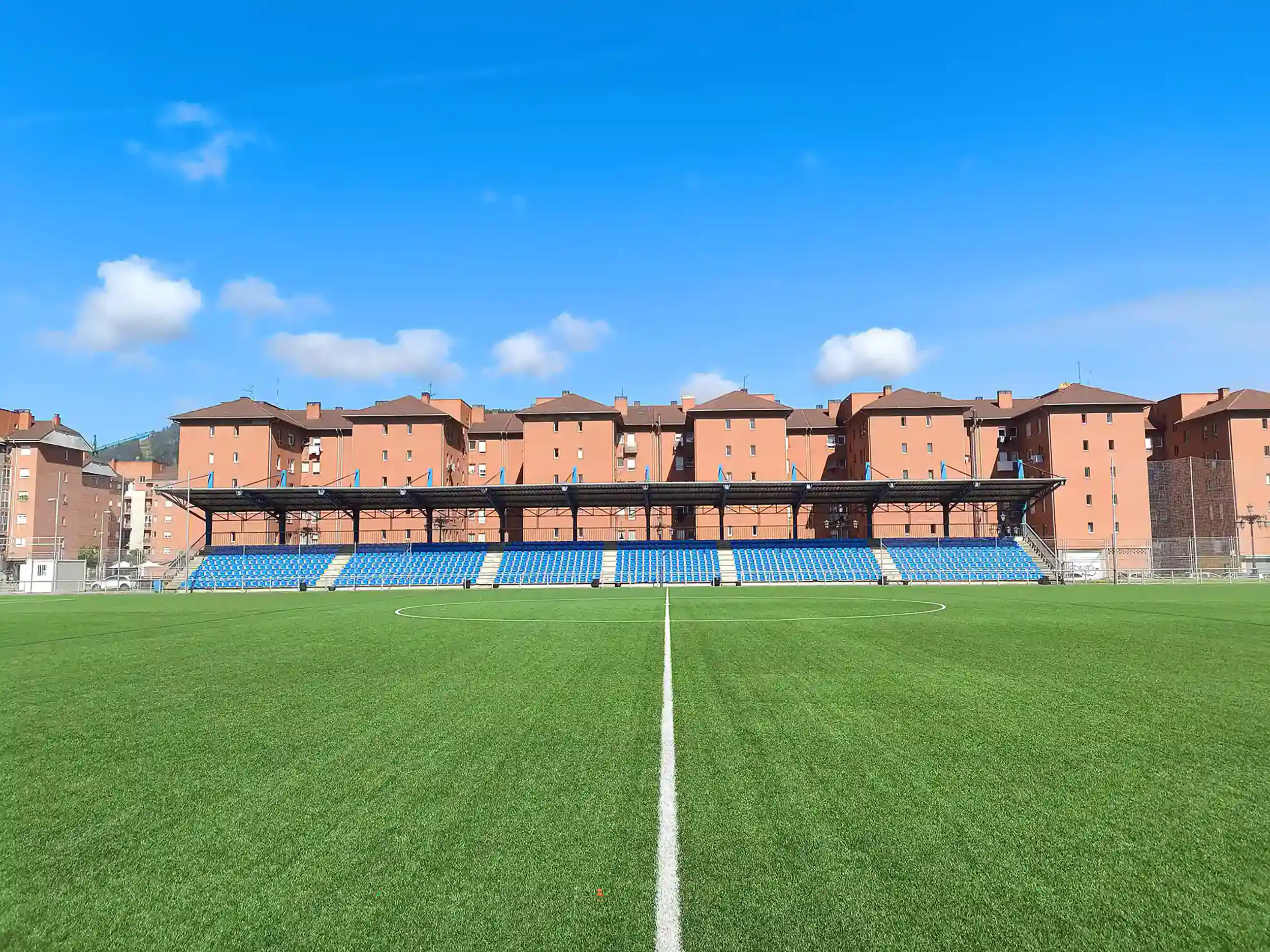 Vista lateral y a pie de campo del terreno de juego, con las gradas y edificios al fondo