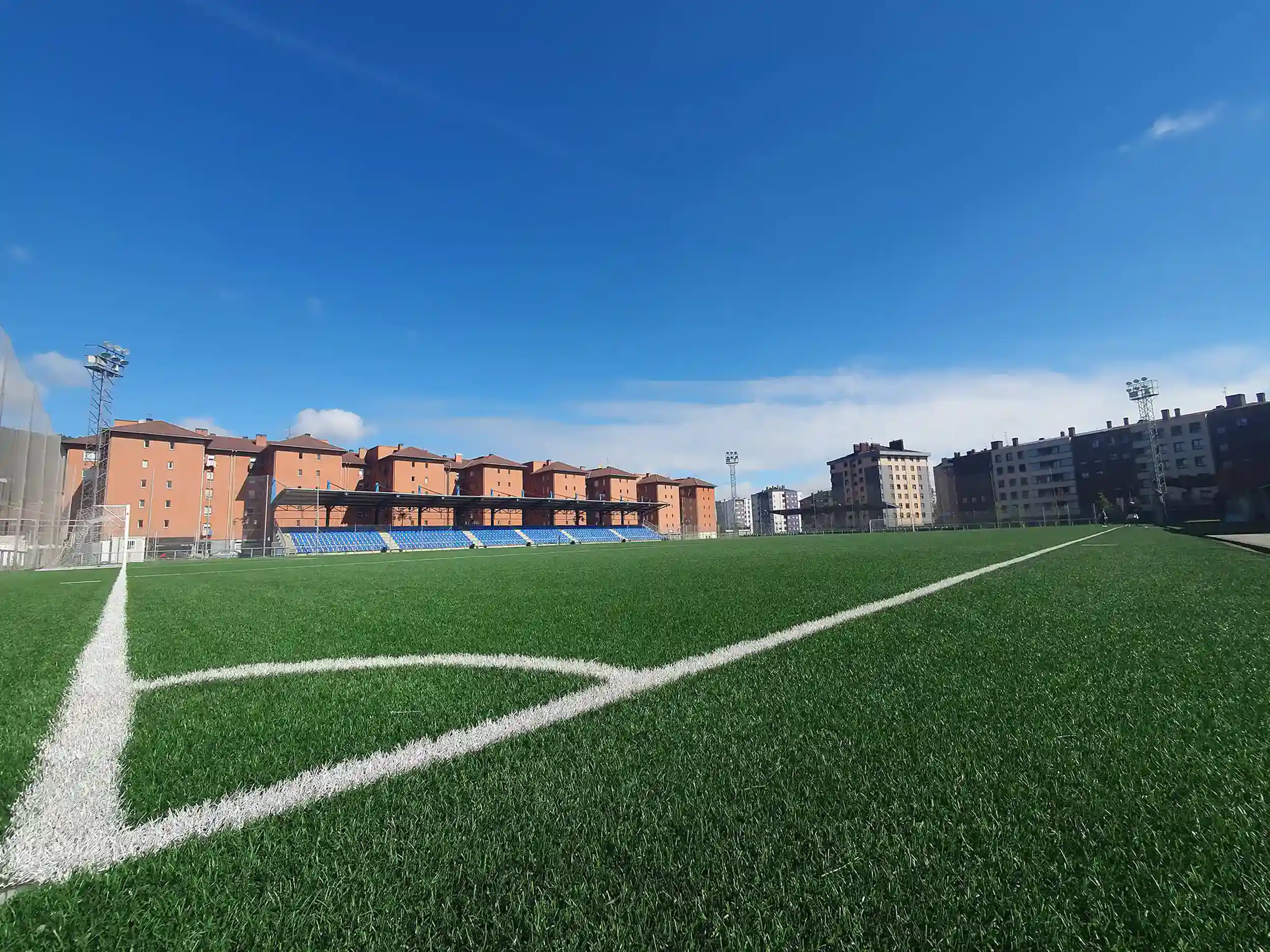 Vista lateral a pie de campo del terreno de juego, desde las líneas del córner. Al fondo, los edificios circundantes