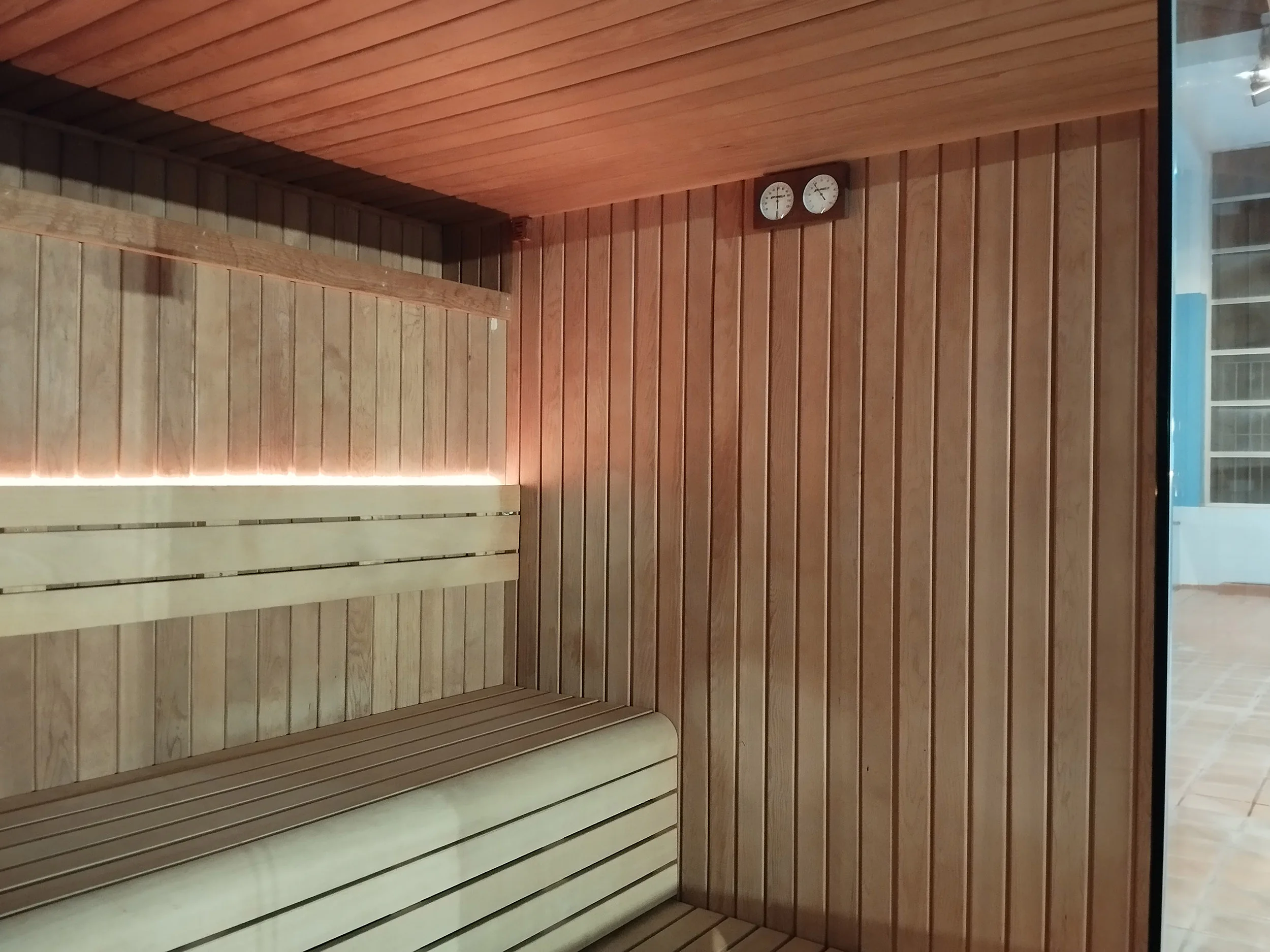 Vista interior de la sauna, con paredes y asientos de madera e indicadores de humedad y temperatura
