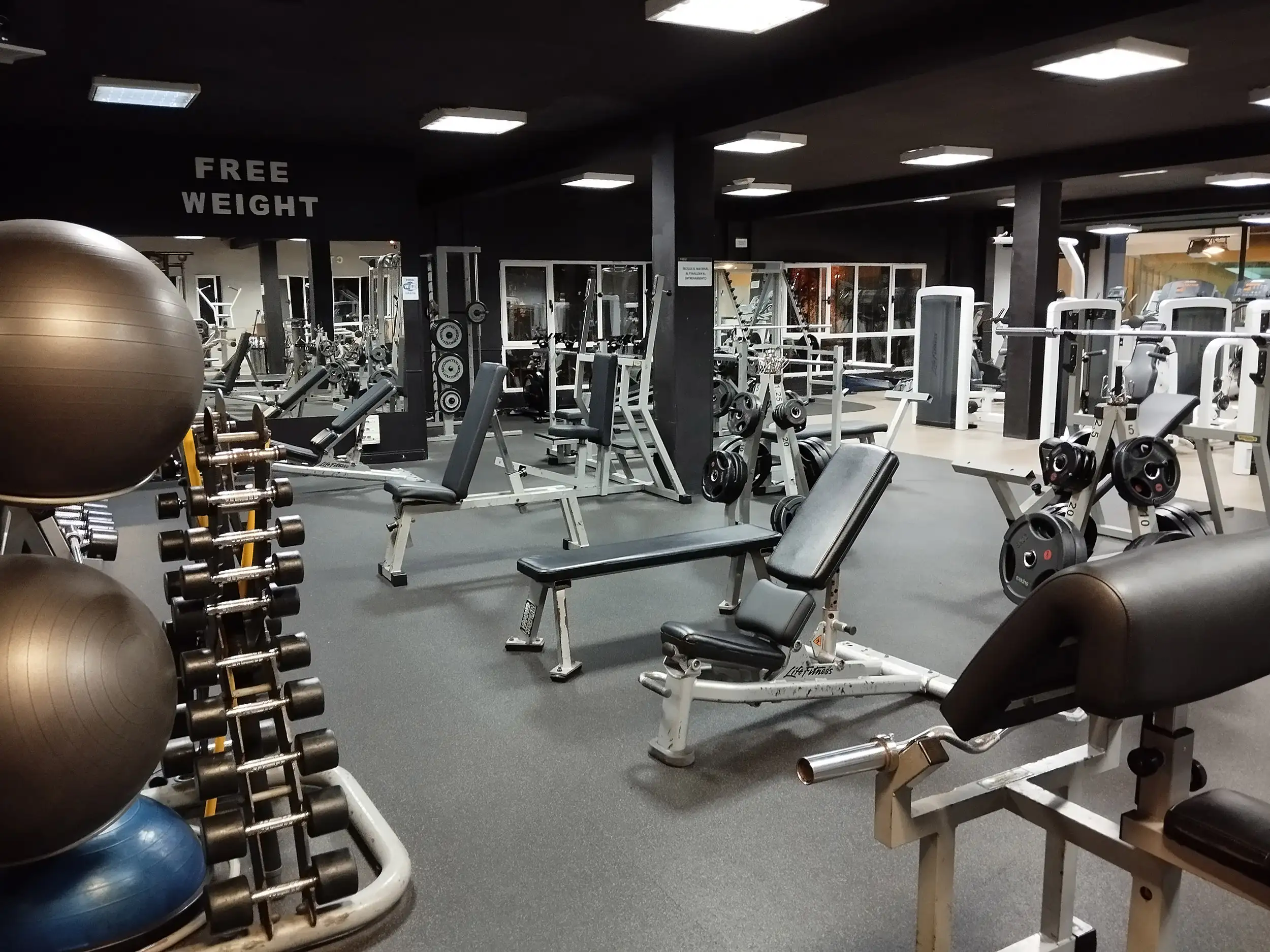 Sala de fitness, con mancuernas en sus soportes y bancos y máquinas de musculación
