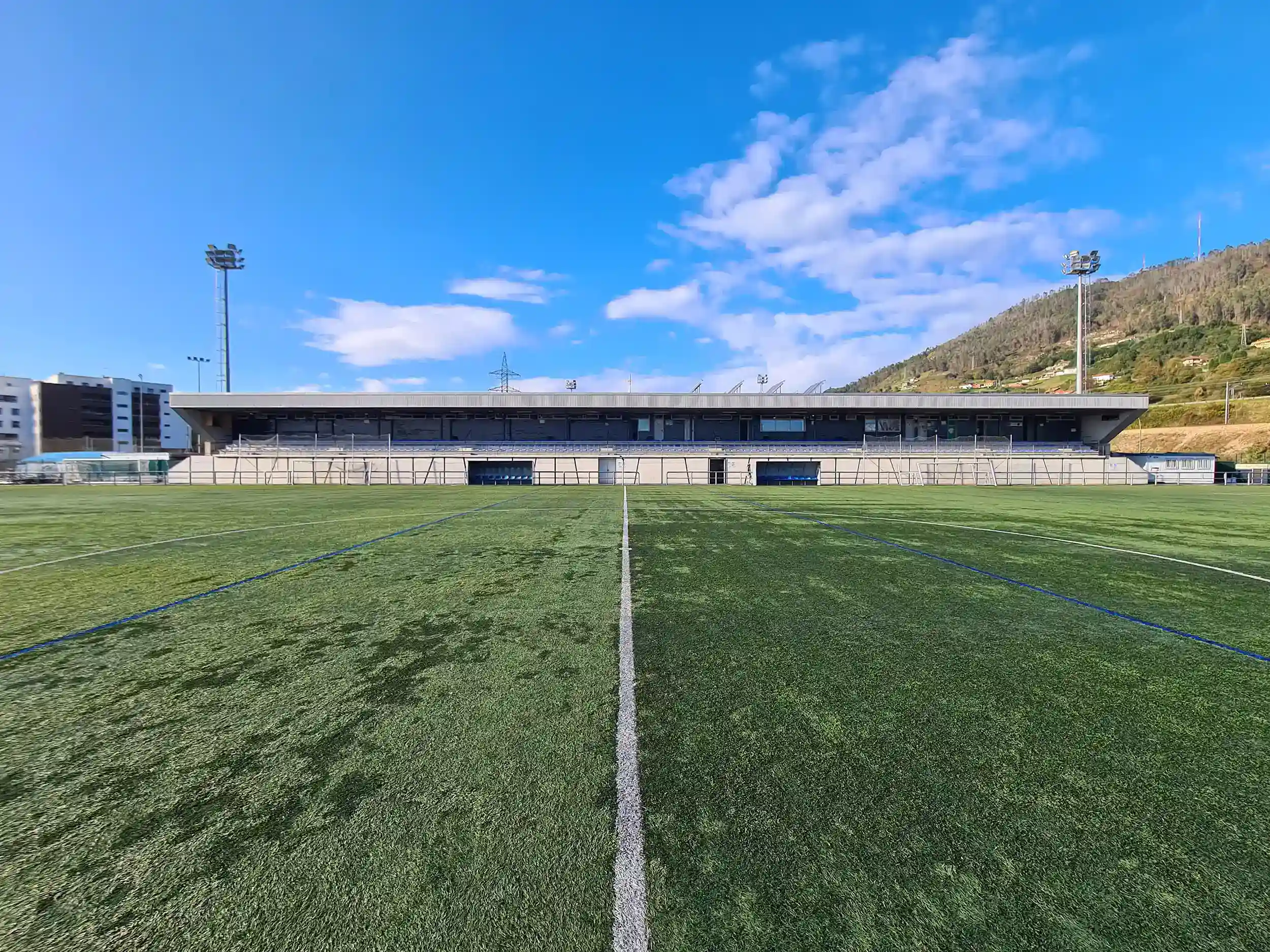 Gradas cubiertas del campo de fútbol desde la línea blanca de medio campo flanqueadas por las torres de iluminación