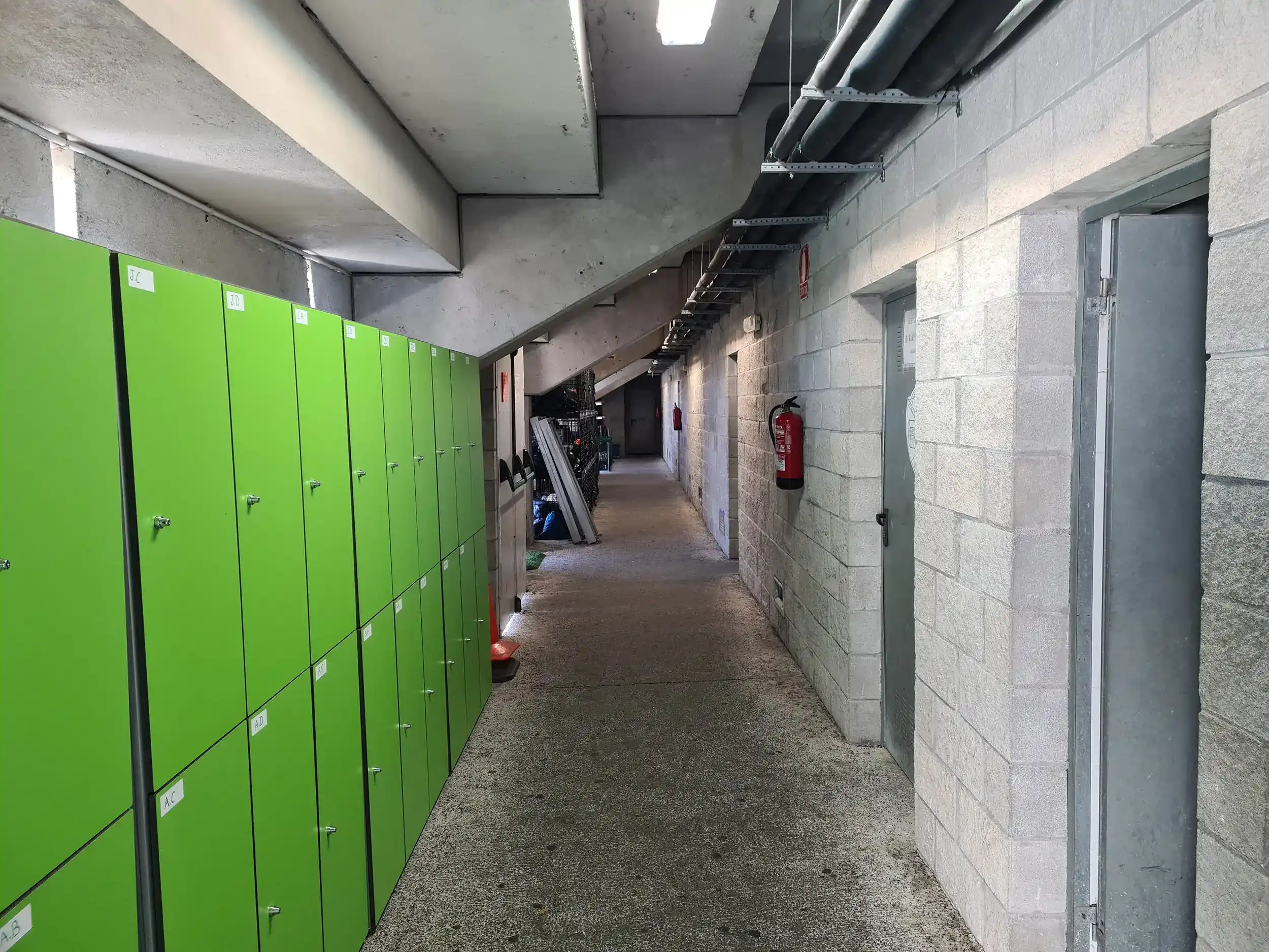 Pasillo con taquillas verdes dispuestas a la izquierda y vestuarios a la derecha