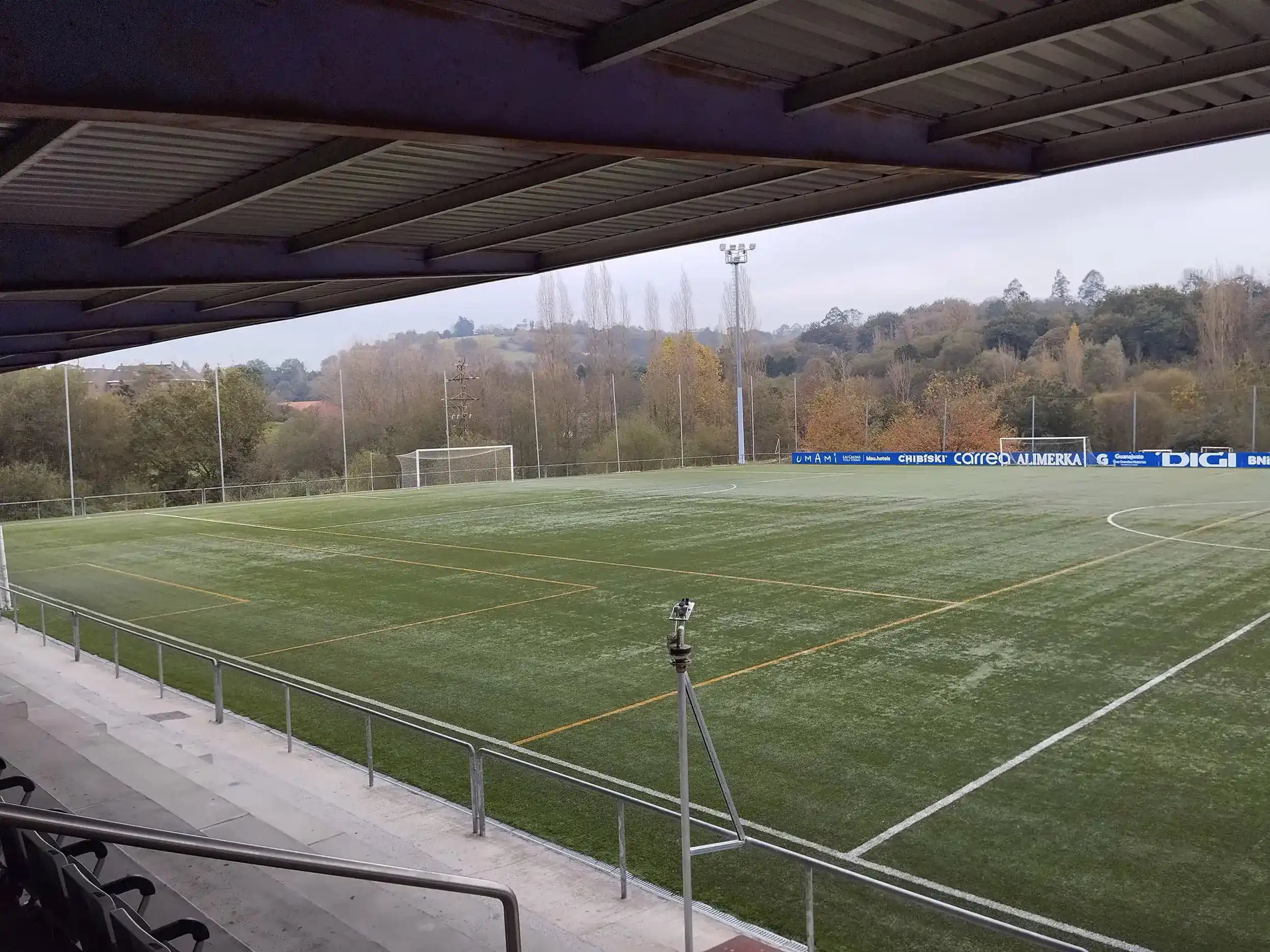 Campo de fútbol visto desde las gradas distinguiéndose la cubierta metalizada y las barandillas plateadas que lo separan