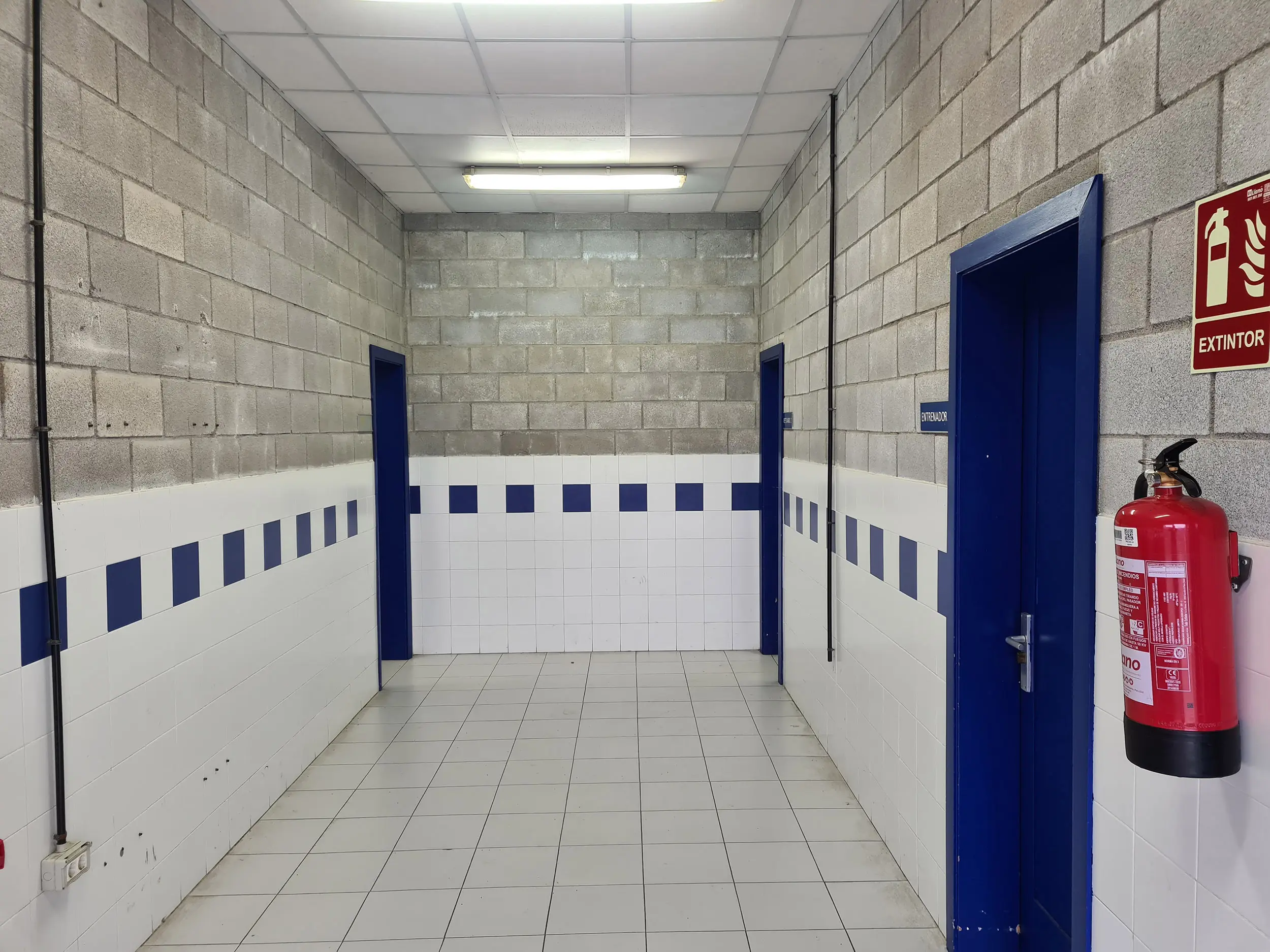 Pasillo interior en color gris con zócalo en color blanco y azul , y puertas azules de acceso a vestuarios