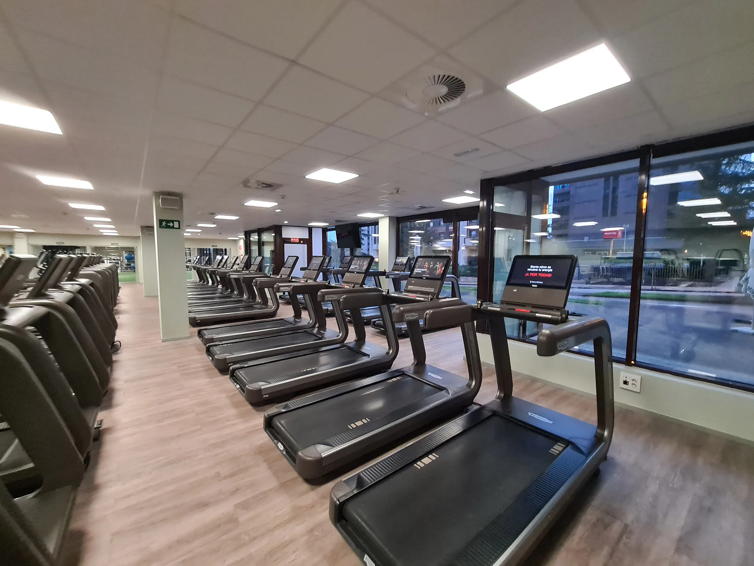 Sala de fitness con una batería de cintas de correr y ventanales al exterior