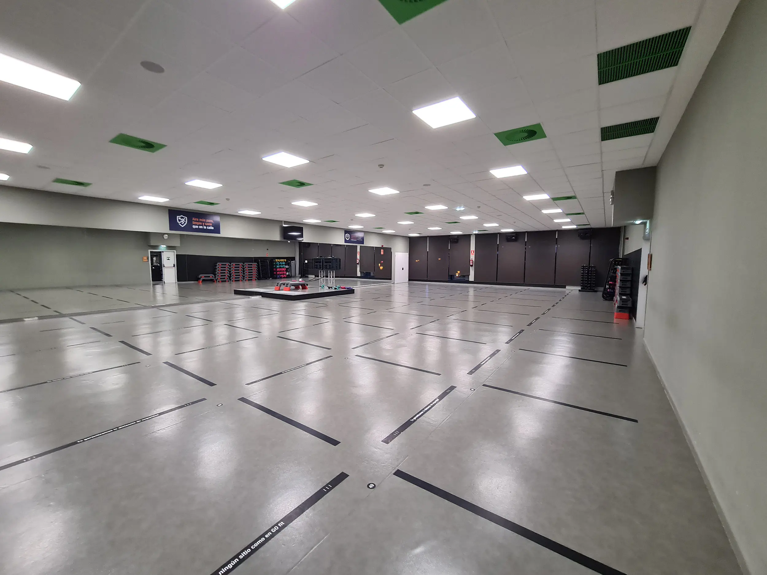 Panorámica general de una de las salas de actividades dirigidas, con diversas pantallas y tarima para el instructor